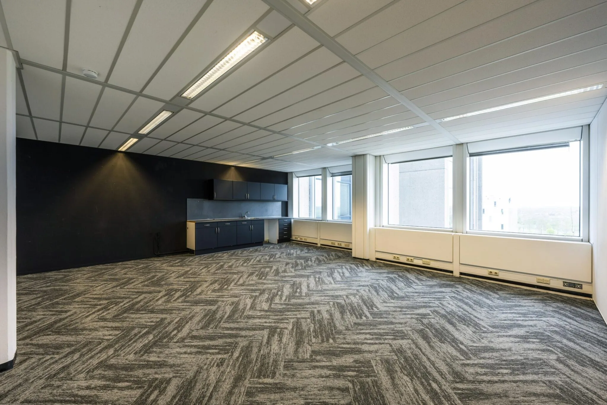 Leeg kantoorpand aan de Laan van Kronenburg met tapijtvloer, systeemplafond, grote ramen en een kitchenette.