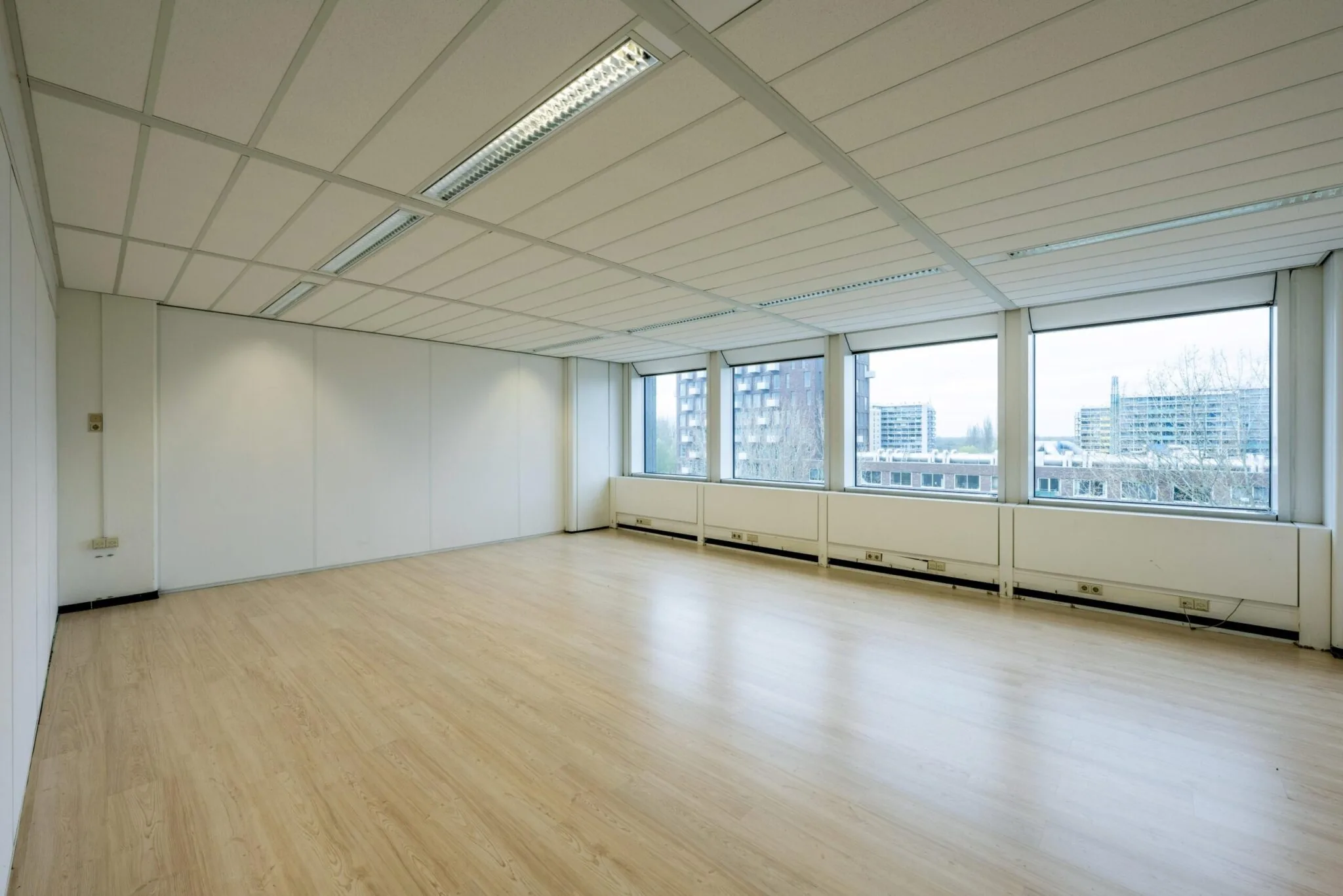 Lege kantoorruimte aan de Laan van Kronenburg met grote ramen en laminaatvloer.