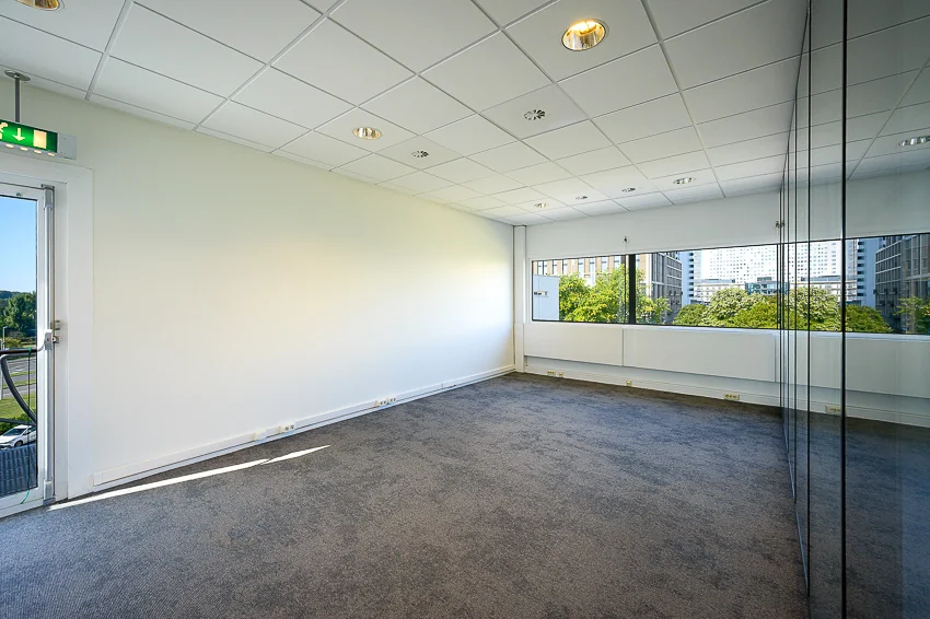 Licht en leeg kantoor met vloerbedekking aan de K.P. van der Mandelelaan, met uitzicht op omliggende gebouwen en bomen.