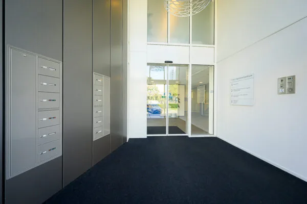 Ingang van een modern kantoorgebouw aan de K.P. van der Mandelelaan met brievenbussen, intercom en automatische schuifdeuren.