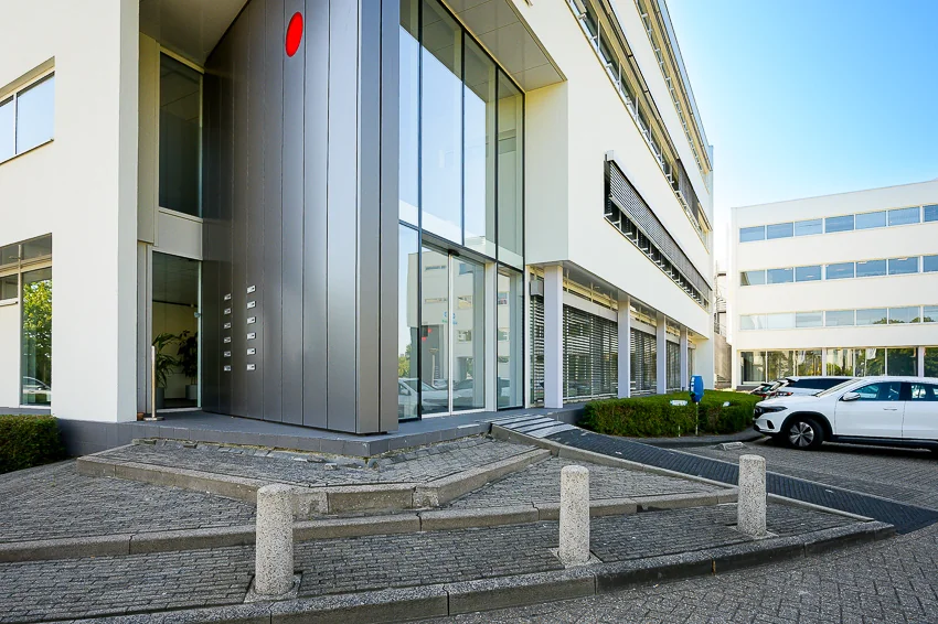 Ingang van een modern kantoorgebouw aan de K.P. van der Mandelelaan met grote ramen en een betegeld toegangspad.