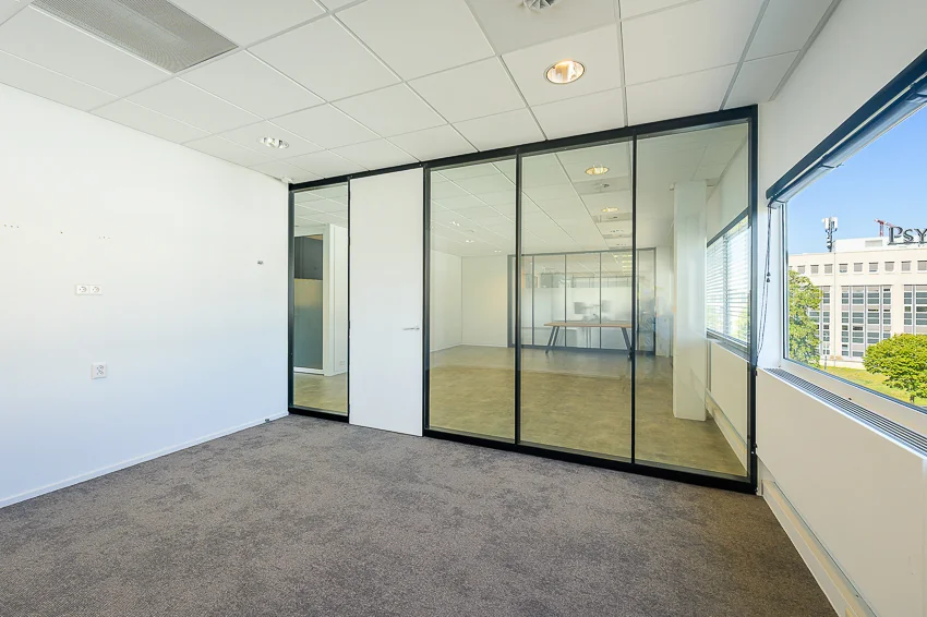 Licht en modern kantoorpand aan de K.P. van der Mandelelaan met glazen scheidingswand en uitzicht op het naastgelegen kantoorgebouw.