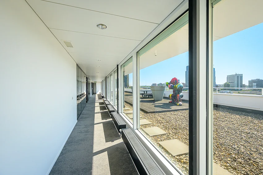 Licht kantoorinterieur met uitzicht op een dakterras aan de K.P. van der Mandelelaan, met een kleurrijk kunstwerk buiten.