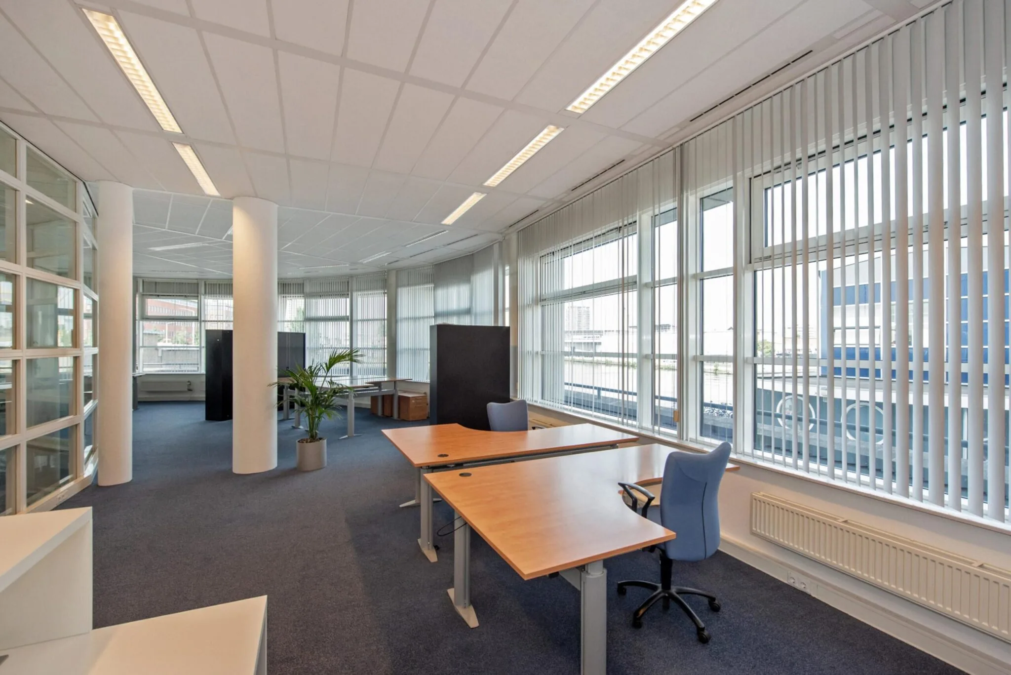 Ruim en licht kantoorinterieur aan de Binckhorstlaan met werkplekken, grote ramen en verticale jaloezieën.