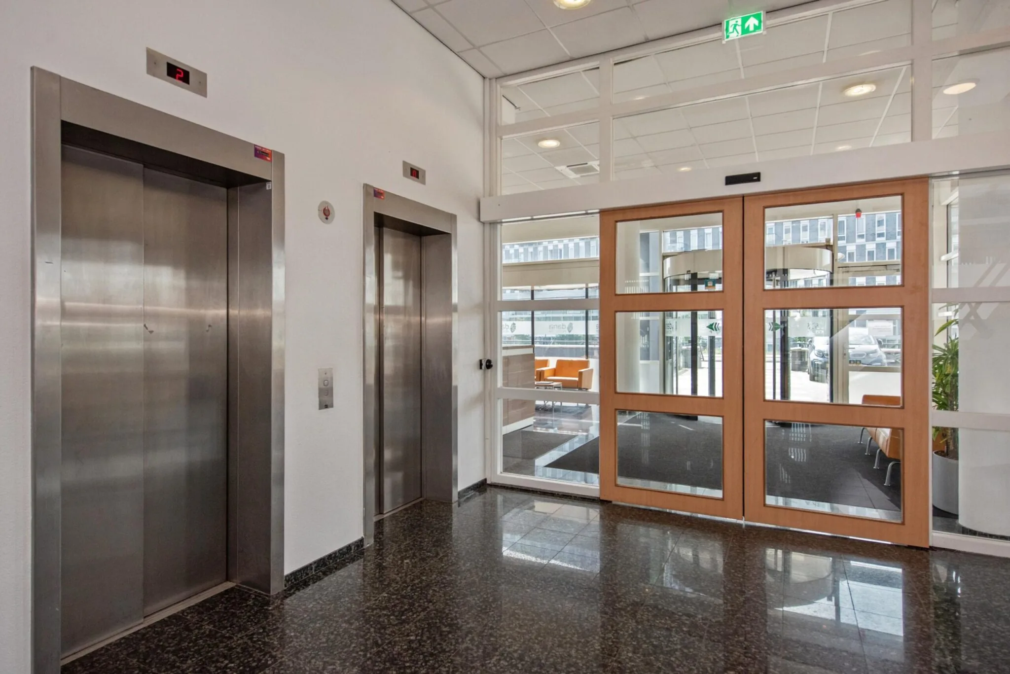 Ingangshal met twee liften en glazen deuren in een kantoorpand aan de Binckhorstlaan.