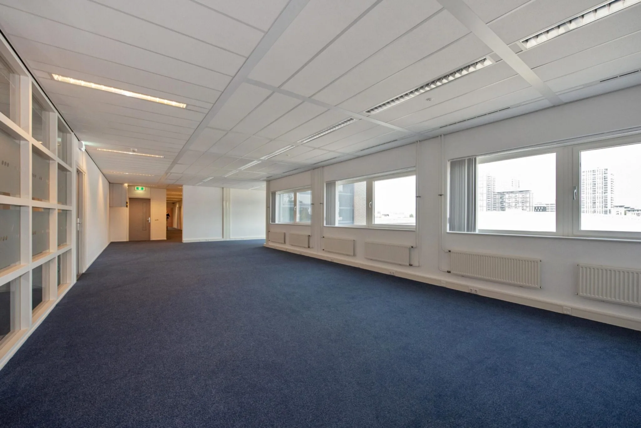 Ruime, lege kantoorruimte aan de Binckhorstlaan met blauwe vloerbedekking en grote ramen.