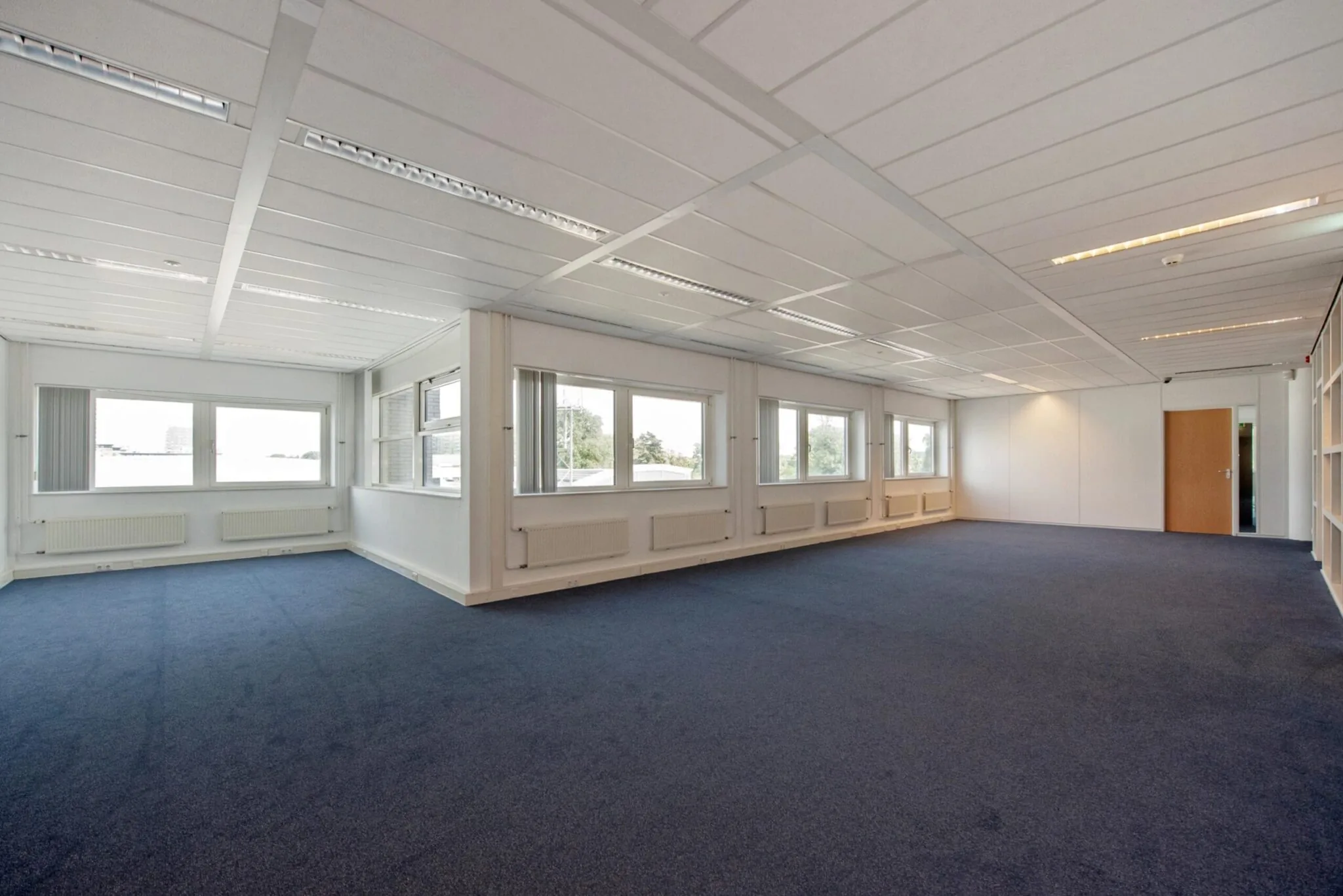 Ruime, lege kantoorruimte aan de Binckhorstlaan met blauwe vloerbedekking en grote ramen.