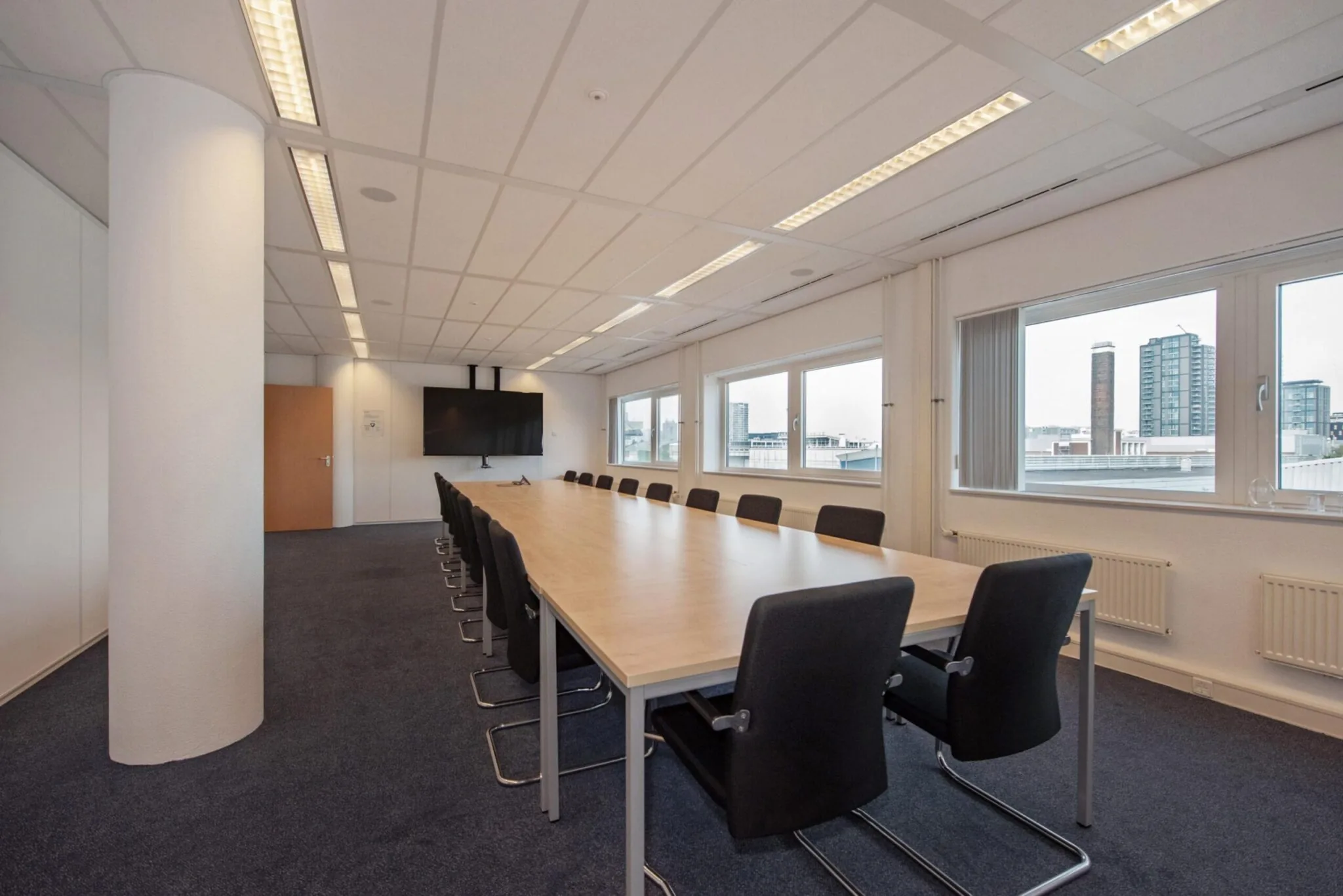 Moderne vergaderruimte aan de Binckhorstlaan met lange tafel, zwarte stoelen en uitzicht op kantoorgebouwen.