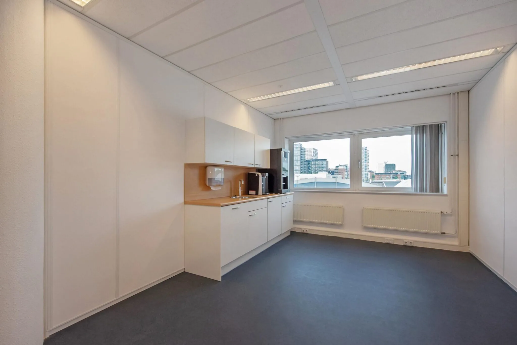 Kleine pantry met koffieautomaat en opbergkasten in een kantoorruimte aan de Binckhorstlaan met uitzicht op de stad.