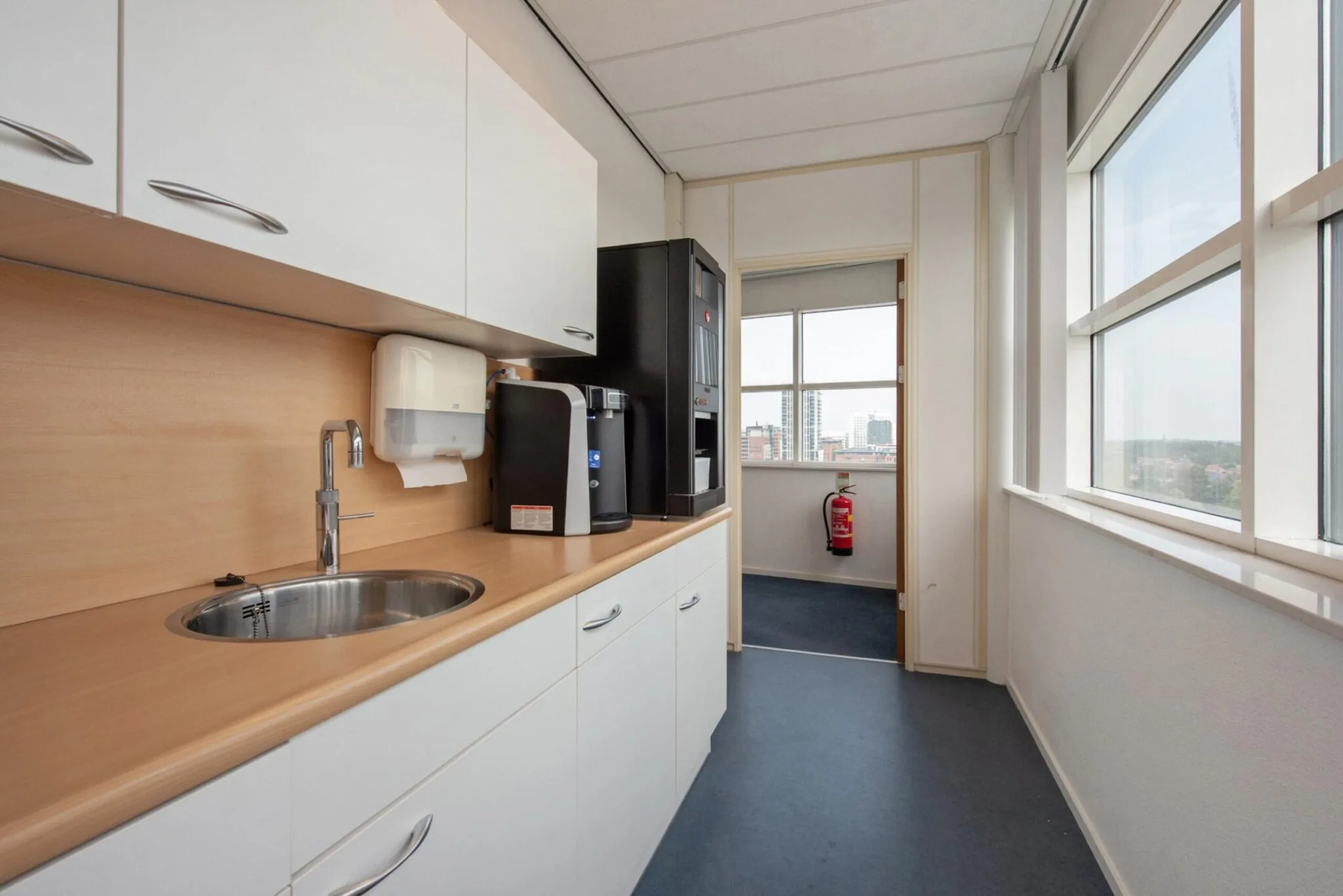 Pantry met koffiezetapparaten, gootsteen en uitzicht op de Binckhorstlaan in een kantoorgebouw.