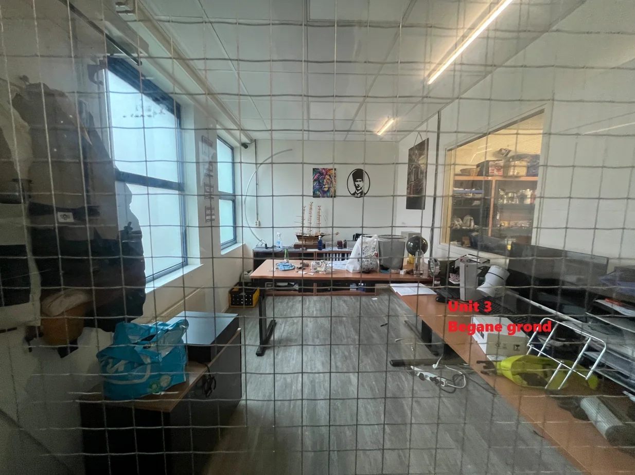 Kantoorruimte met bureaus, kasten en decoraties gezien door een roosterdeur, met de tekst "Unit 3 Begane grond" in rood.