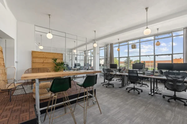 Een moderne open kantoorruimte met houten scheidingswanden, bureaus en ergonomische stoelen, verlicht door grote ramen.