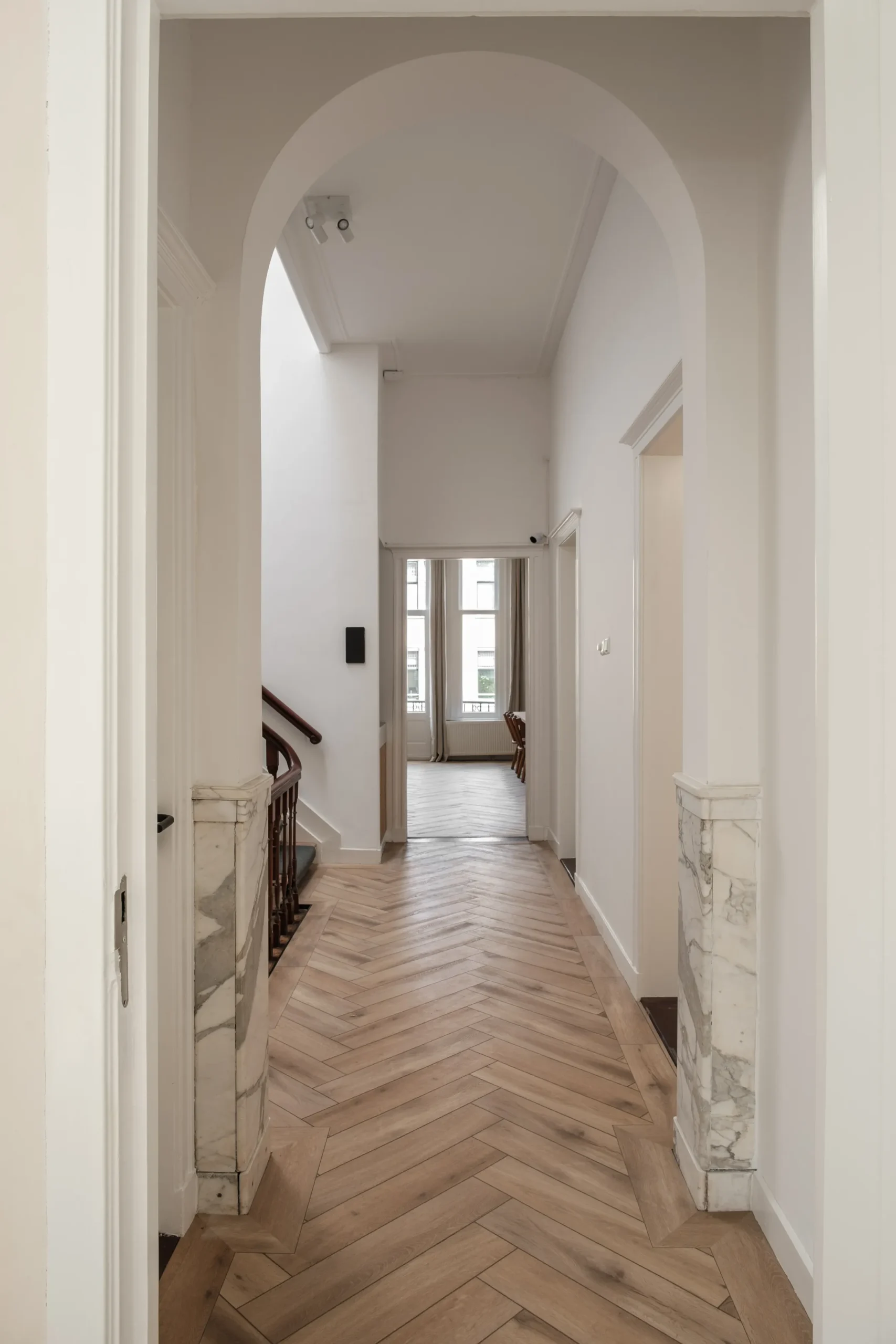 Elegant ganginterieur met houten visgraat vloer en marmeren details.