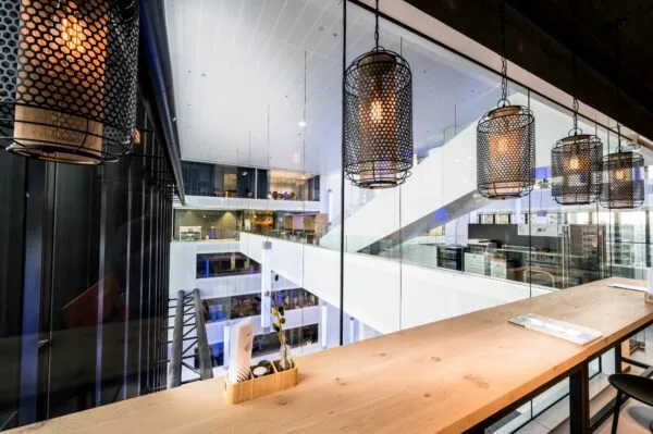 Moderne kantoorruimte met uitzicht op een open atrium en hangende industriële lampen boven een houten werktafel.