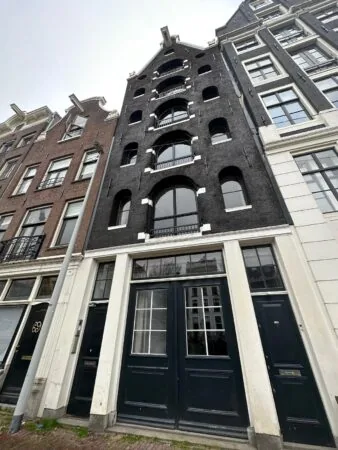 Voorgevel van een smal, zwart herenhuis aan de Herengracht in Amsterdam met ronde ramen en witte kozijnen.