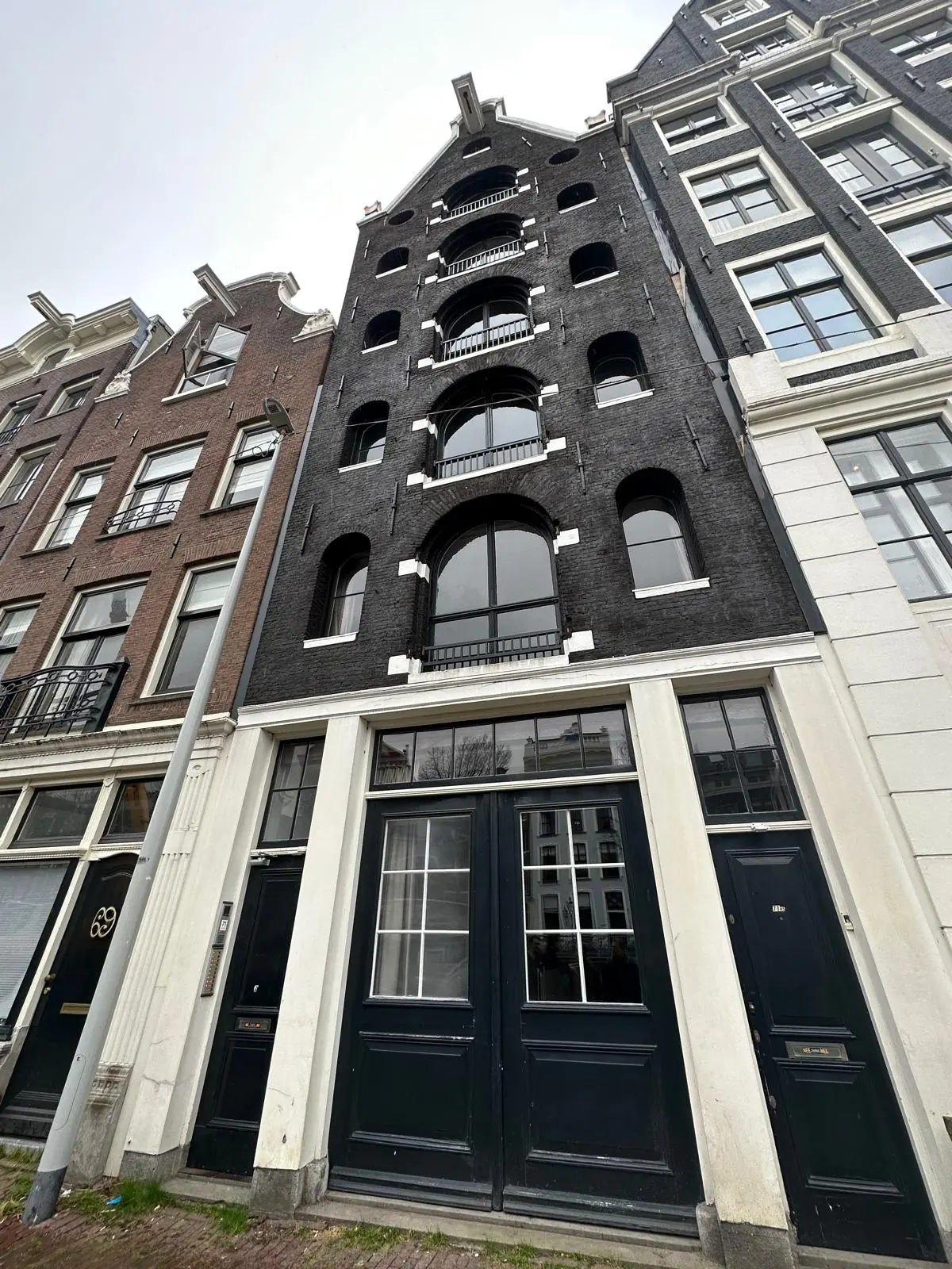 Voorgevel van een smal, zwart herenhuis aan de Herengracht in Amsterdam met ronde ramen en witte kozijnen.