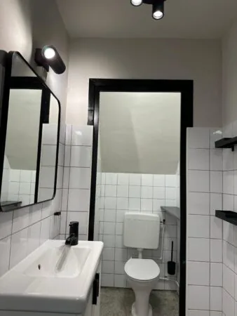 Moderne, wit betegelde toiletruimte aan de Herengracht met zwart-witte accenten, wastafel en wandspots.