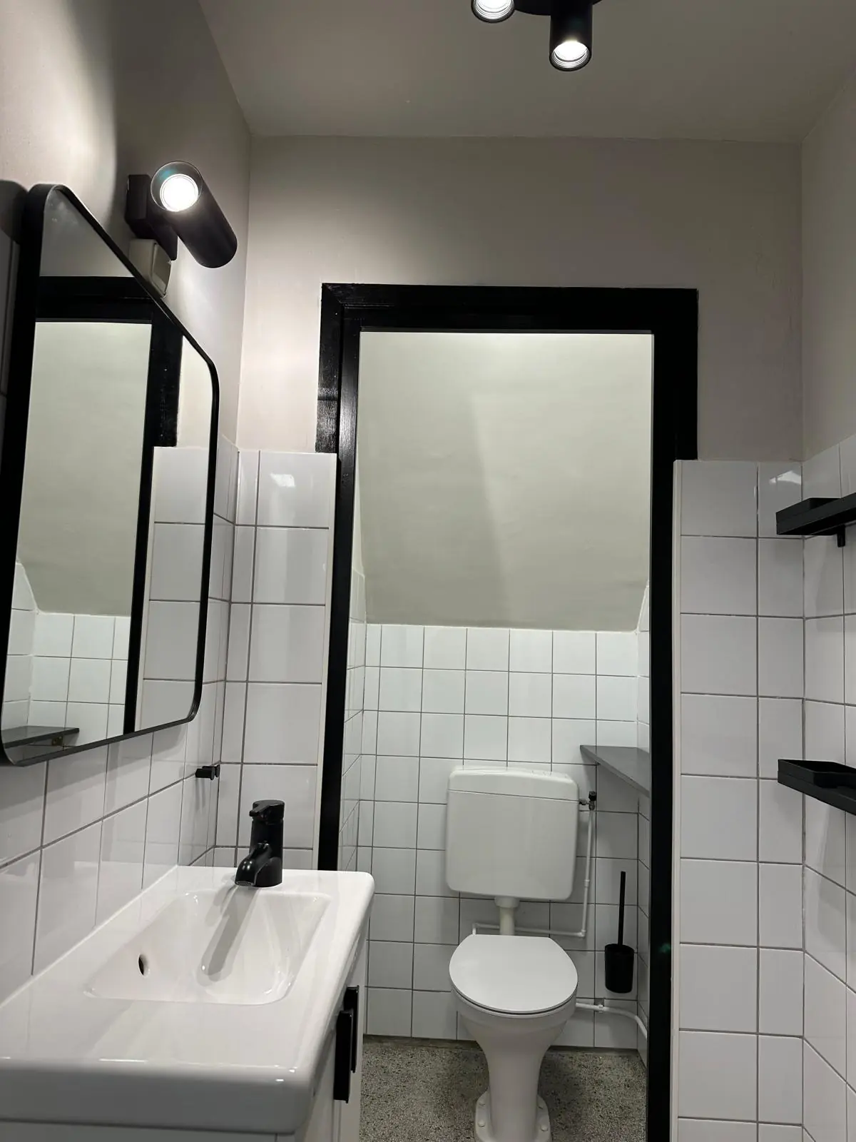 Moderne, wit betegelde toiletruimte aan de Herengracht met zwart-witte accenten, wastafel en wandspots.