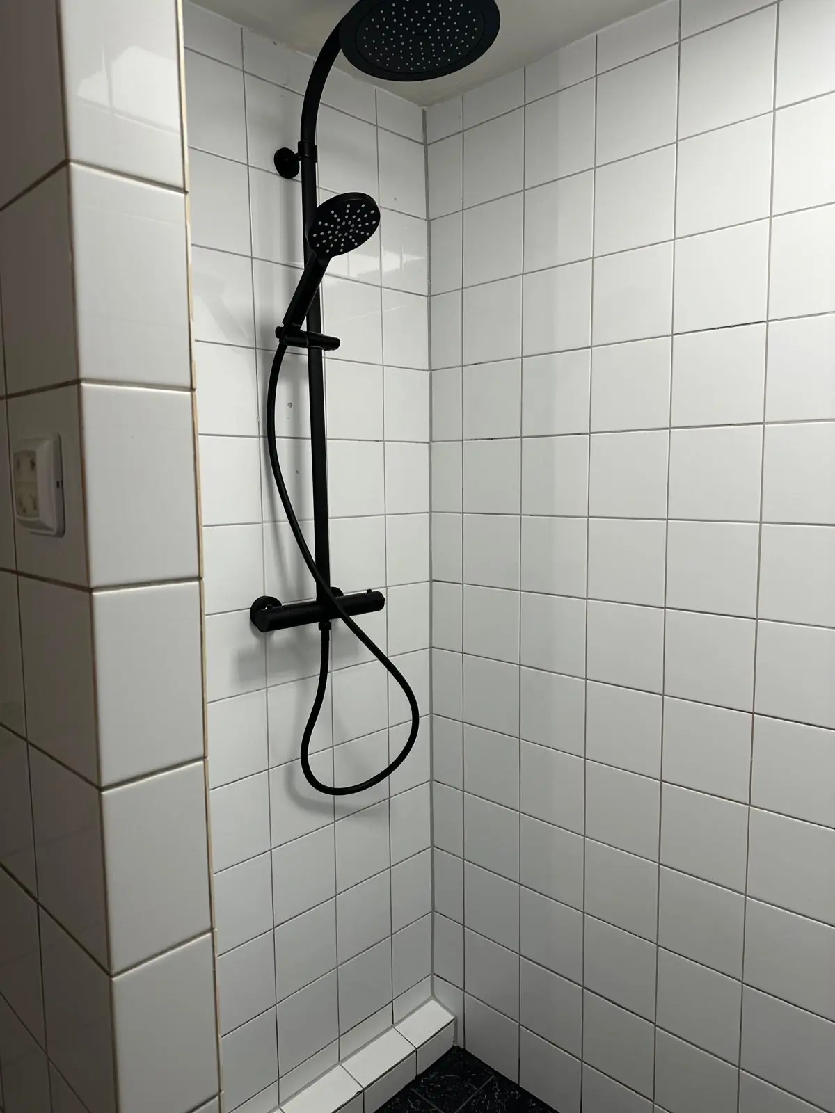 Moderne douche met zwarte regendouche en handdouche in een betegelde witte douchecabine op Herengracht.