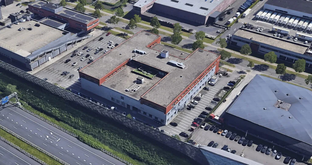 Luchtfoto van het bedrijfsgebouw aan de Proostwetering met parkeerplaats, gelegen langs de snelweg.