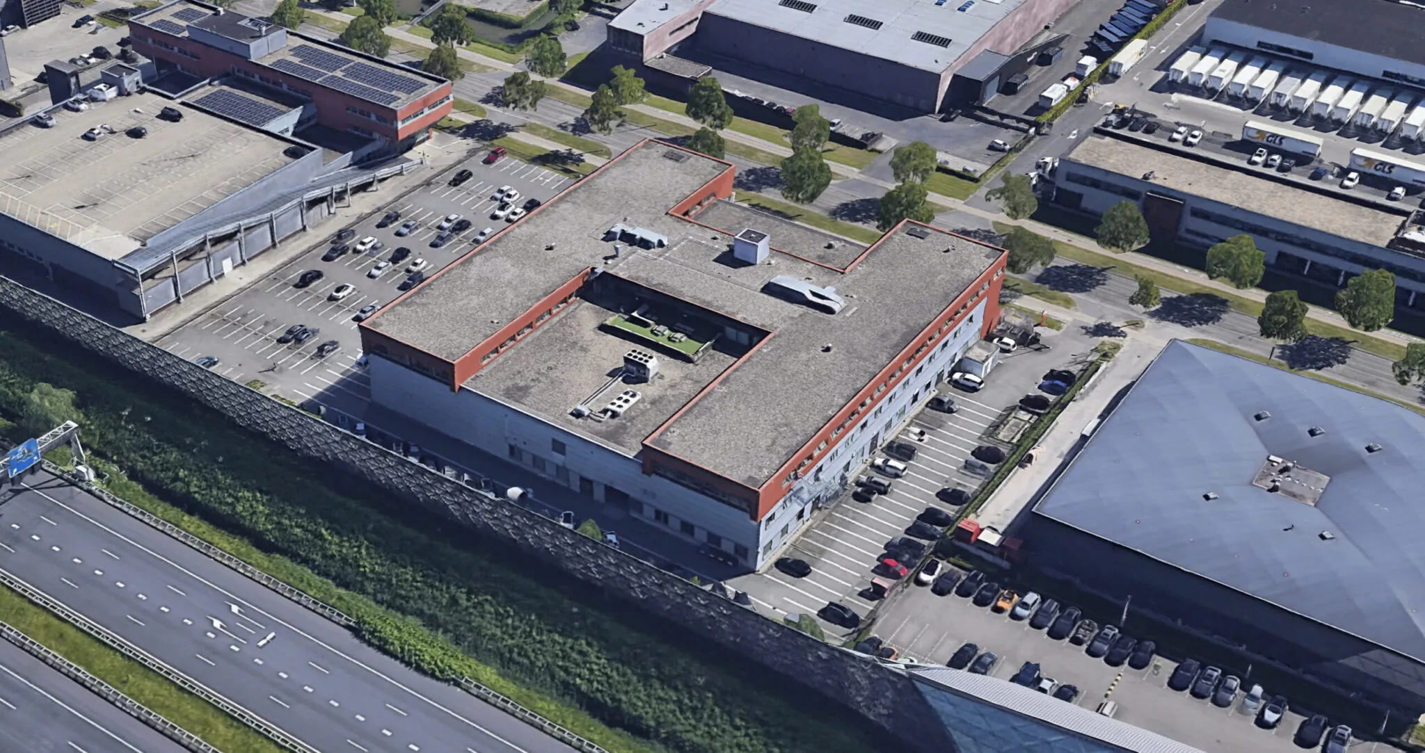 Luchtfoto van het bedrijfsgebouw aan de Proostwetering met parkeerplaats, gelegen langs de snelweg.