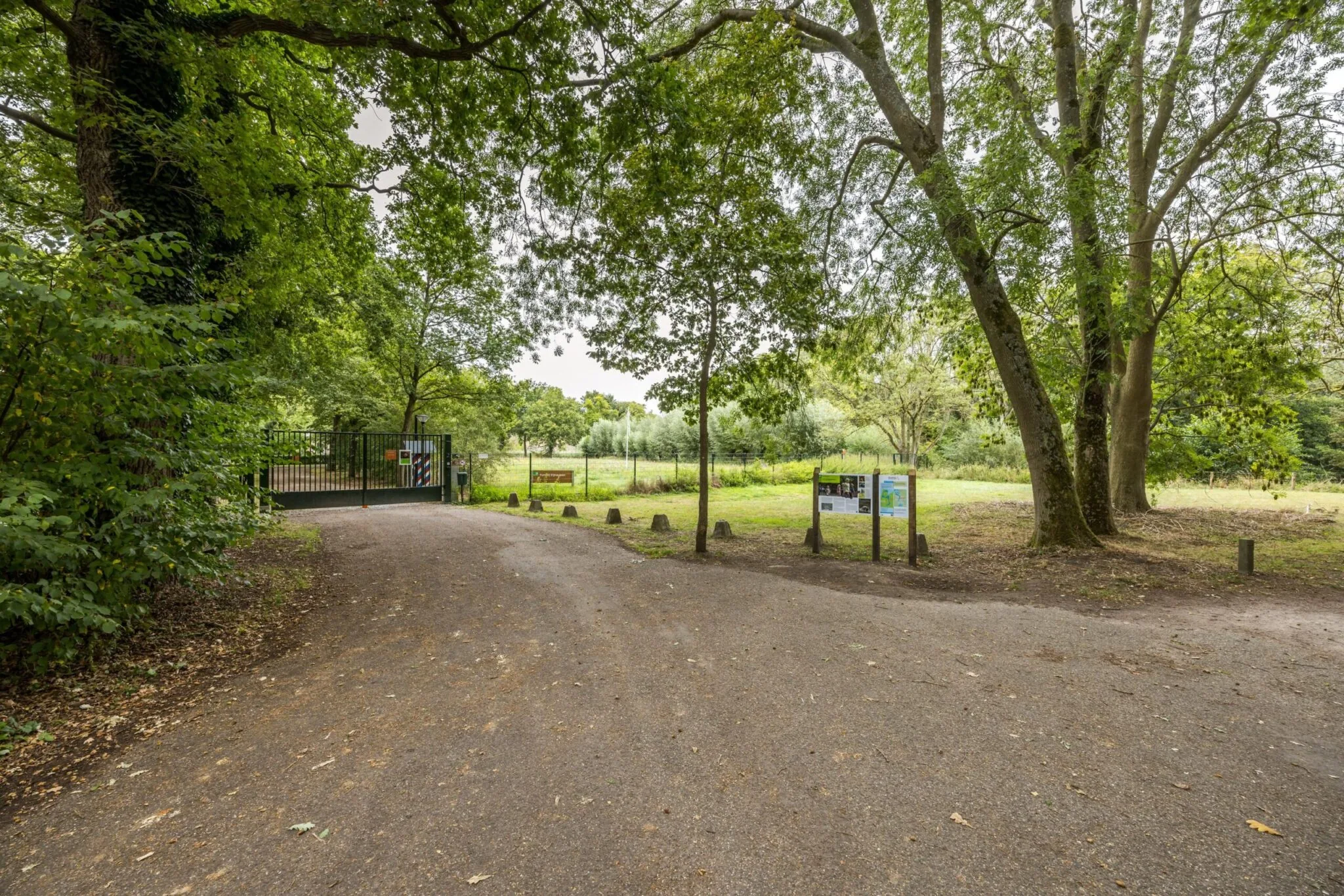 Ingang van een groen natuurgebied aan de Vossegatsedijk met een afgesloten hek en informatieve borden langs het pad.