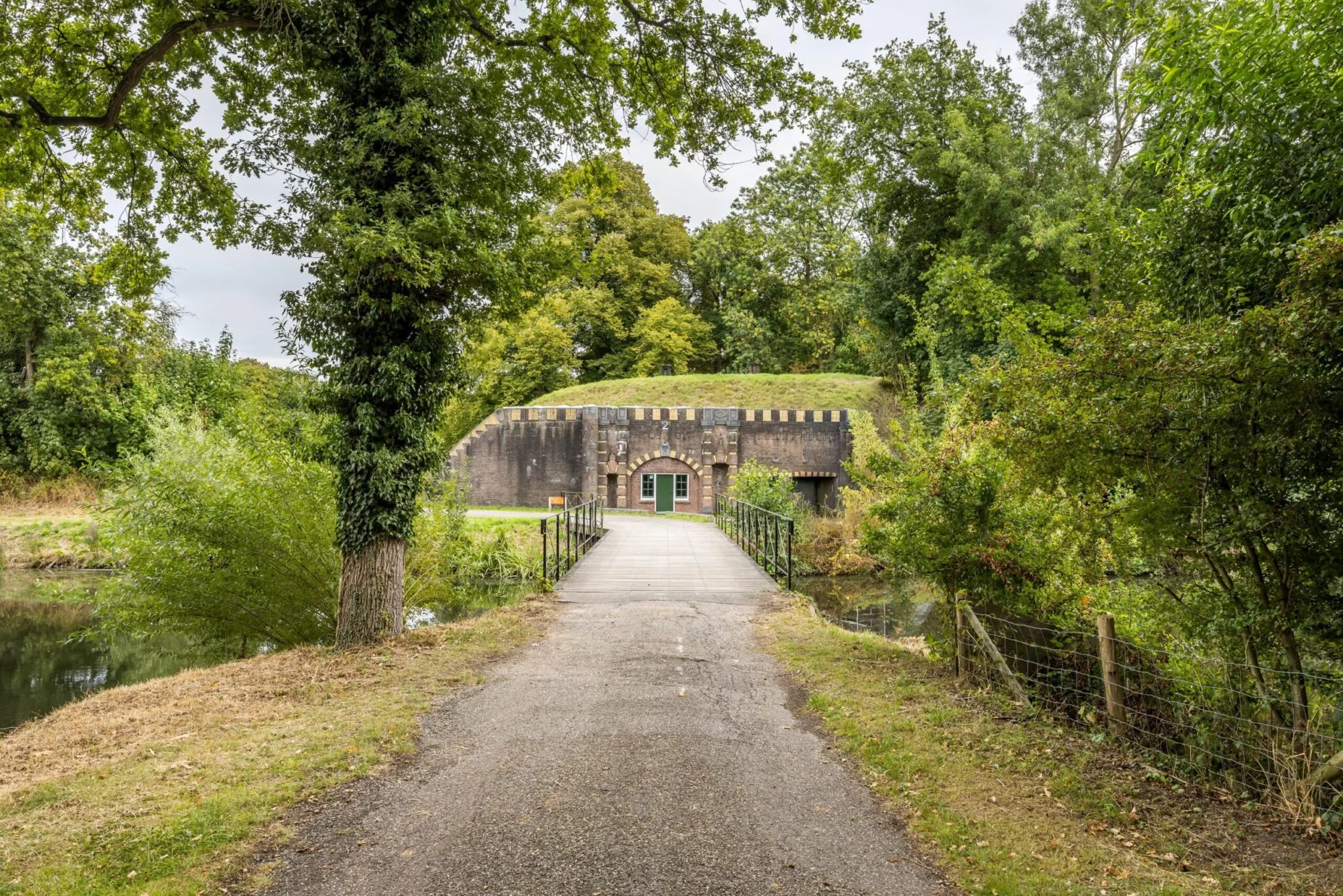 Vooraanzicht van Fort bij Rijnauwen aan de Vossegatsedijk, omringd door groen en bereikbaar via een smalle brug.