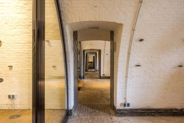 Doorkijk in een gang met bakstenen gewelven en witte muren in een historisch pand aan de Vossegatsedijk.