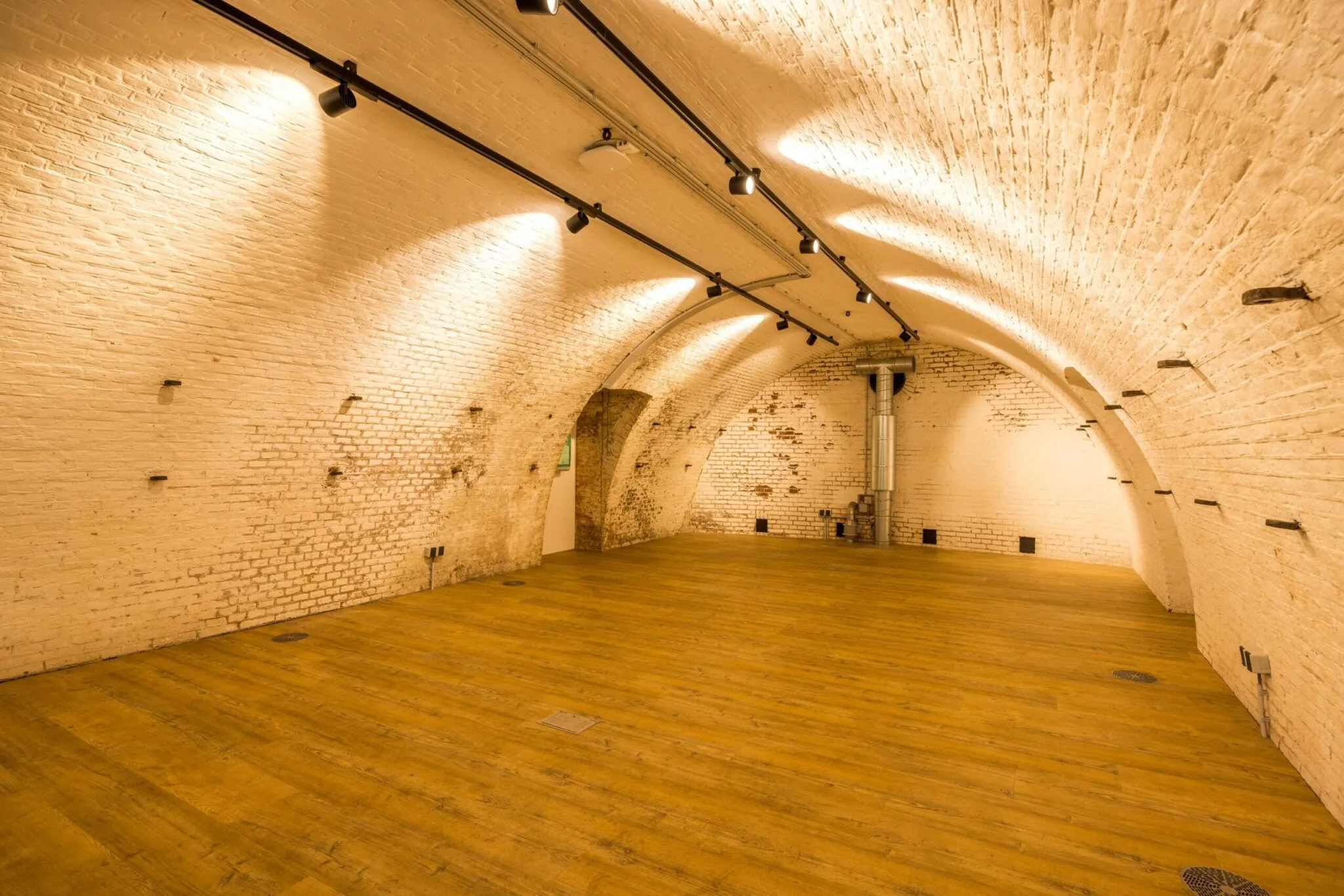 Gewelfde bakstenen kelderruimte aan de Vossegatsedijk met houten vloer en moderne verlichting.