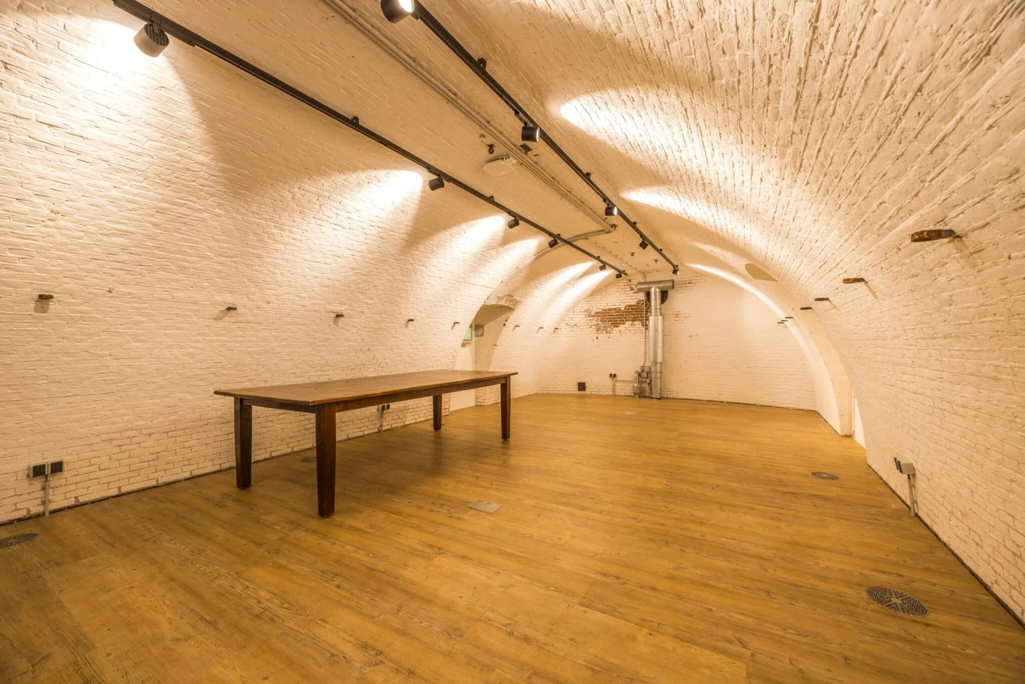 Kelderruimte met gewelven aan de Vossegatsedijk, met witgeschilderde bakstenen muren, houten vloer en een houten tafel.