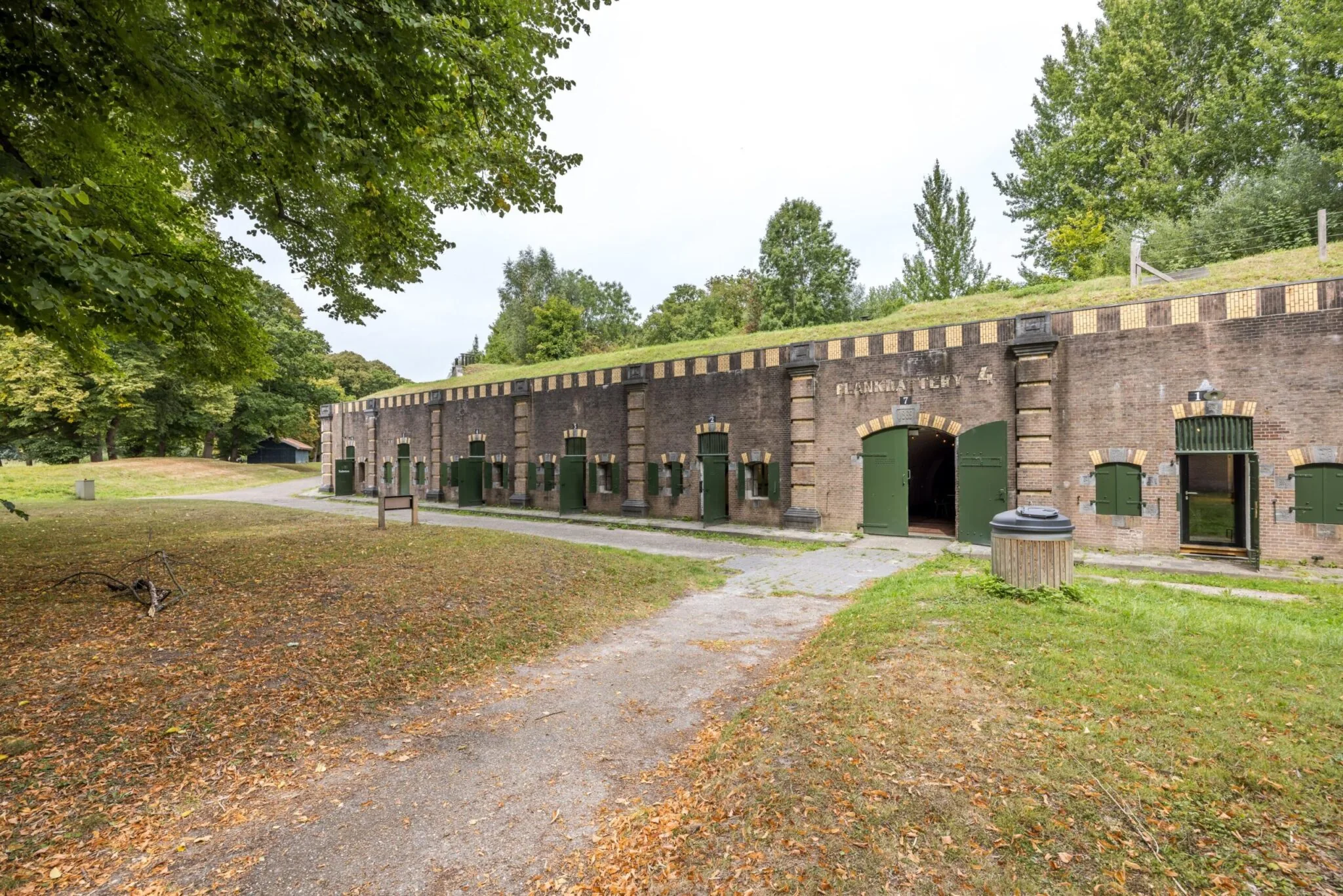 Historisch fortgebouw aan de Vossegatsedijk met groene deuren en omringd door bomen.