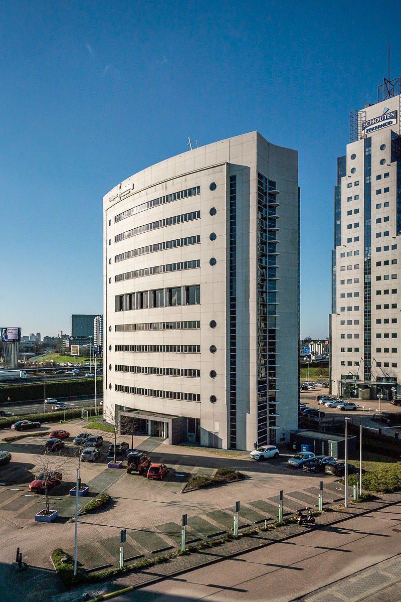 Een modern kantoorgebouw in het Rivium Quadrant met parkeerplaatsen op de voorgrond en een heldere blauwe lucht.