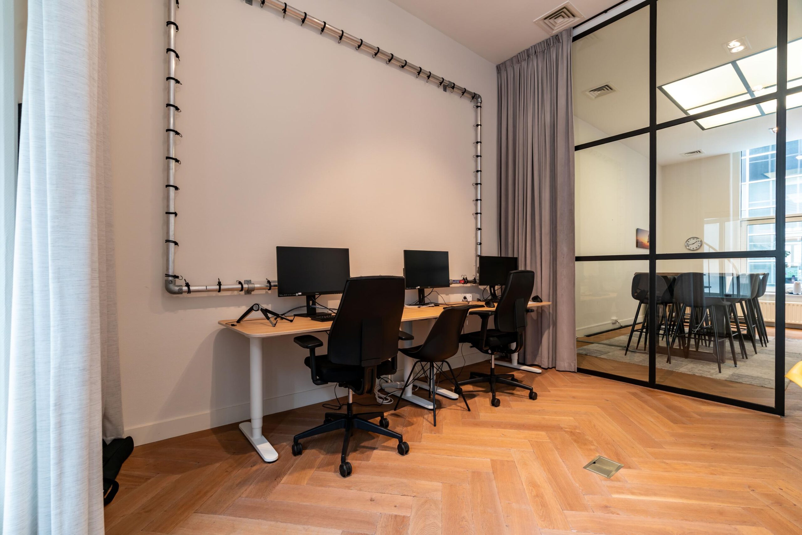 Moderne kantoorruimte aan de Lange Vijverberg met drie werkplekken en een vergaderruimte achter een glazen wand.