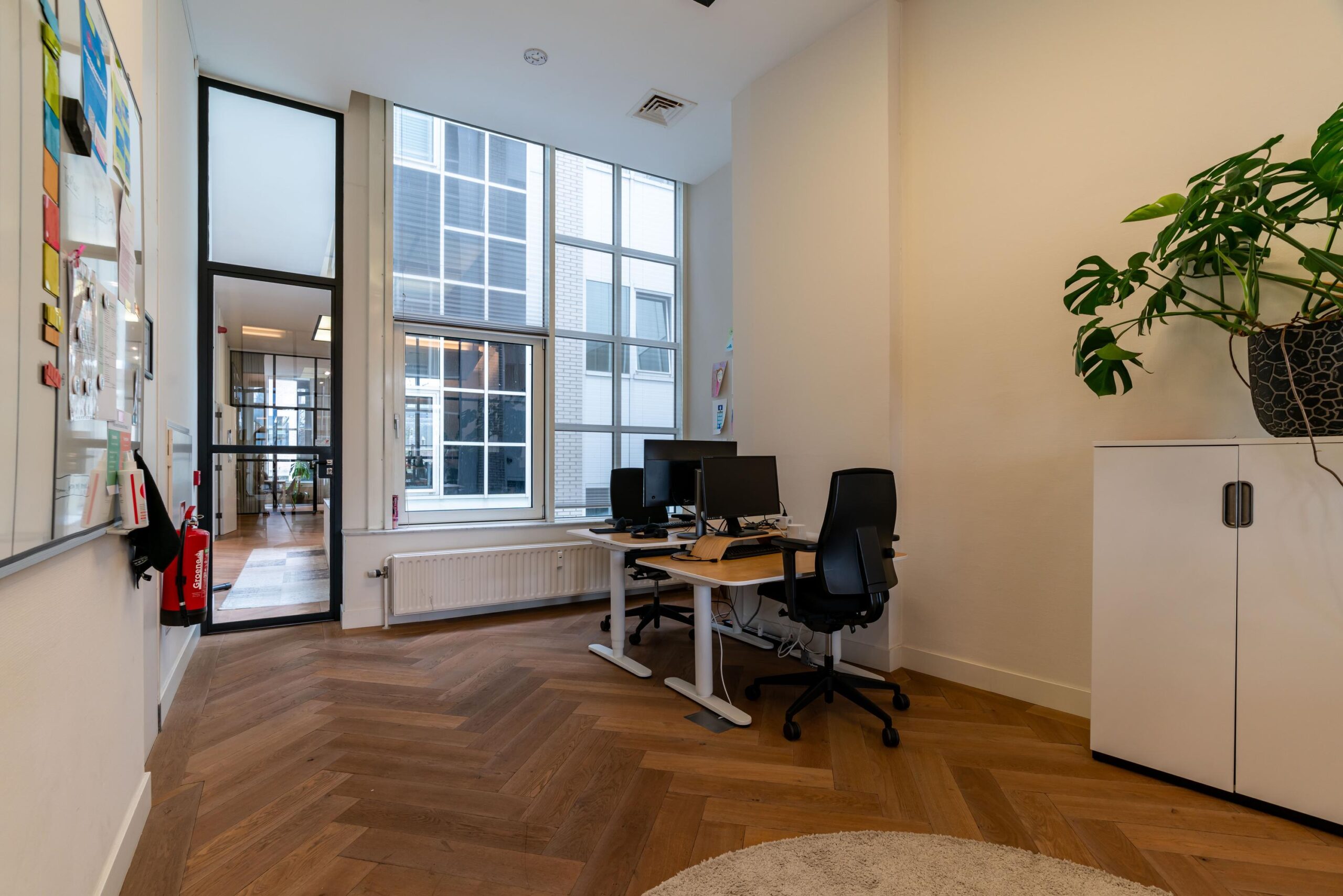 Modern kantoorinterieur aan de Lange Vijverberg met houten visgraatvloer, bureaus met computers en grote ramen met uitzicht op een binnenplaats.