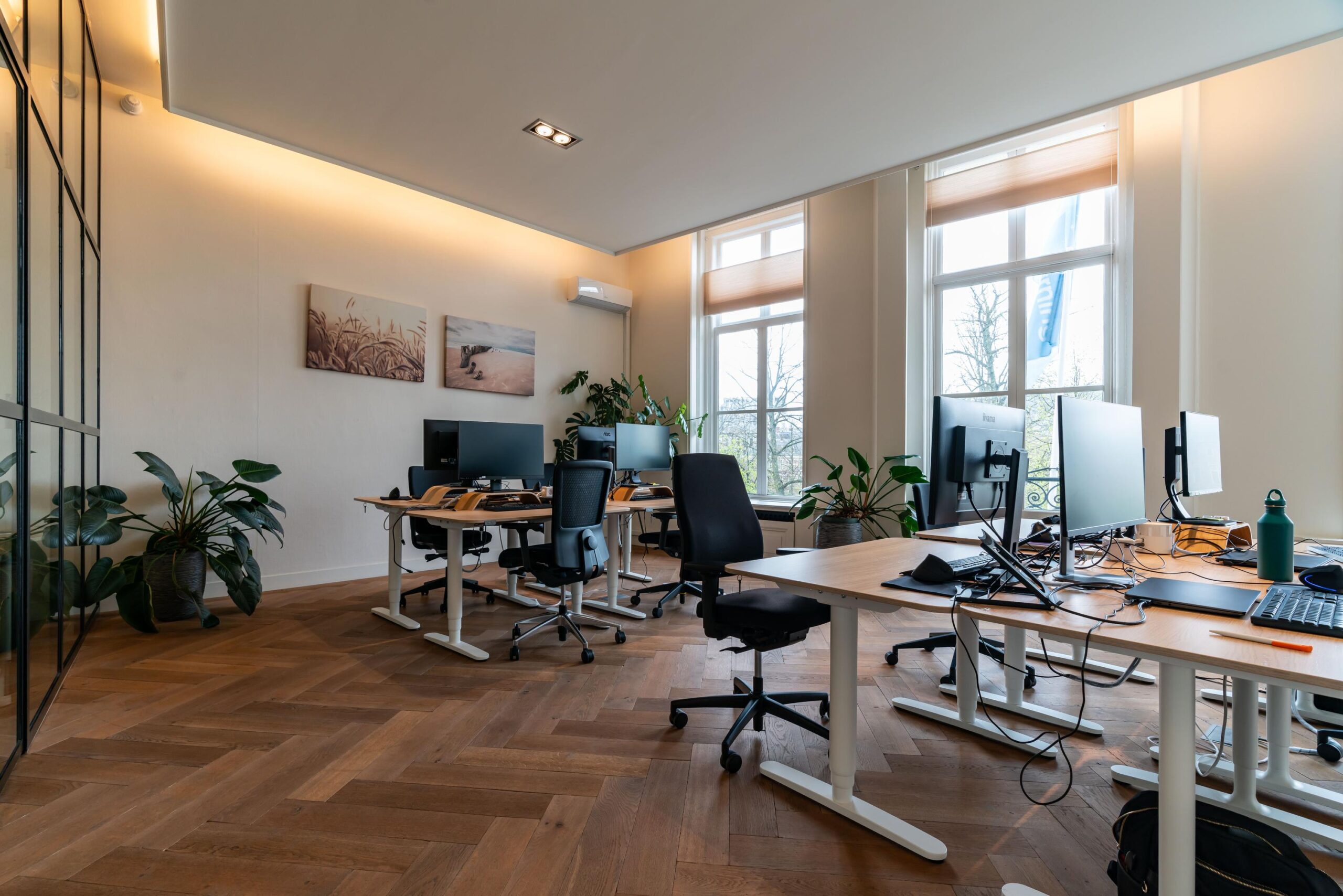 Modern kantoorinterieur aan de Lange Vijverberg met bureaus, computers, planten en grote ramen met uitzicht naar buiten.