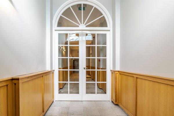 Hal met witgelakte dubbele deur met glas-in-loodramen en houten lambrisering in het gebouw aan de Lange Vijverberg.