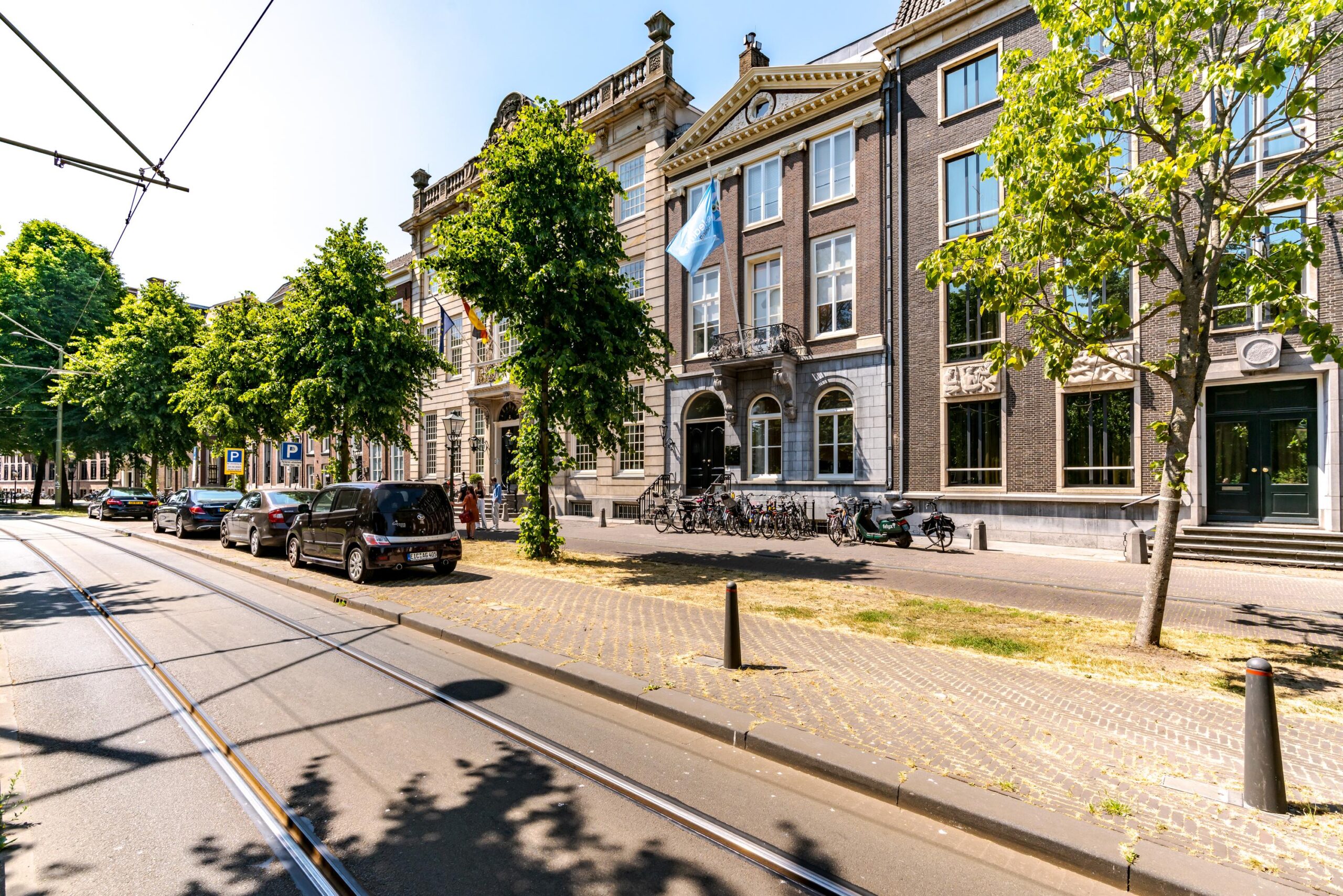 Straatbeeld van de Lange Vijverberg in Den Haag met historische panden, geparkeerde auto's en tramlijnen.