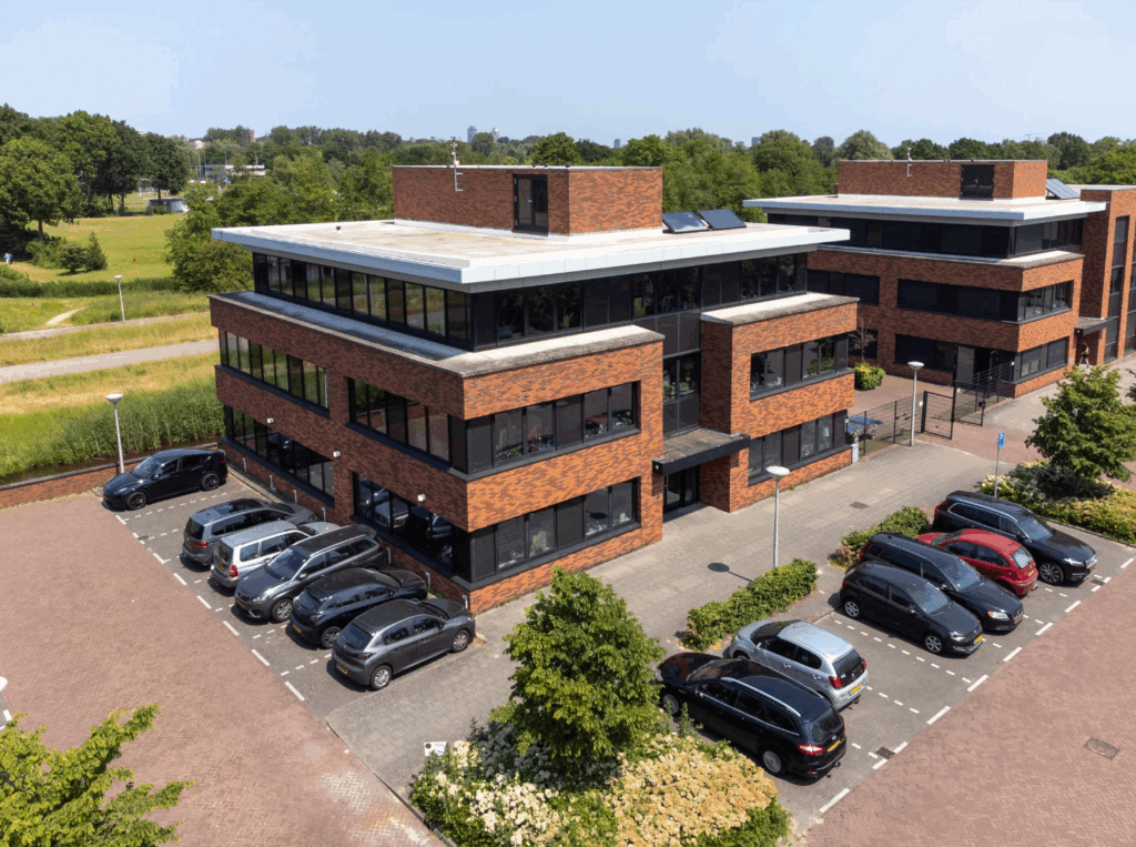 Luchtfoto van een modern kantoorpand aan de Veteranenlaan met omliggende parkeerplaatsen en groenstroken.