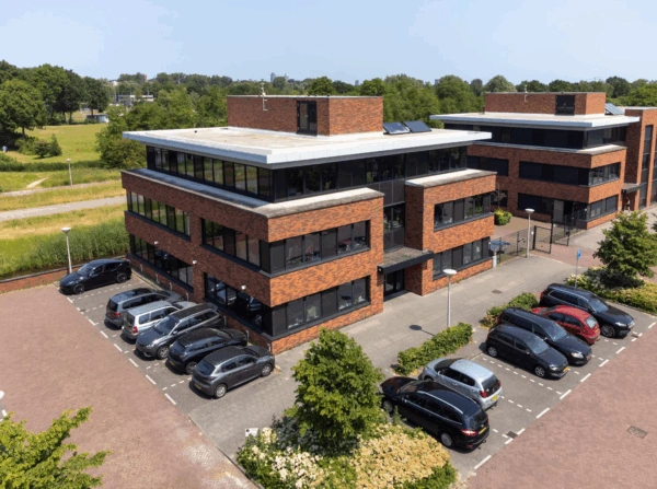 Luchtfoto van een modern kantoorpand aan de Veteranenlaan met omliggende parkeerplaatsen en groenstroken.