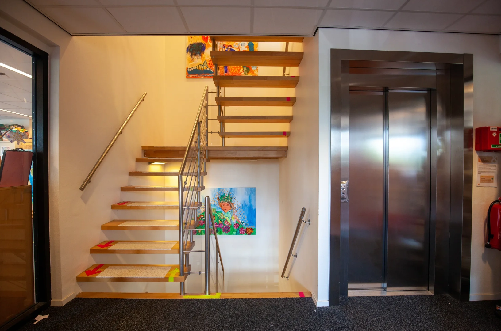 Trap en lift in een kleurrijk trappenhuis aan de Veteranenlaan, met schilderijen aan de muur.