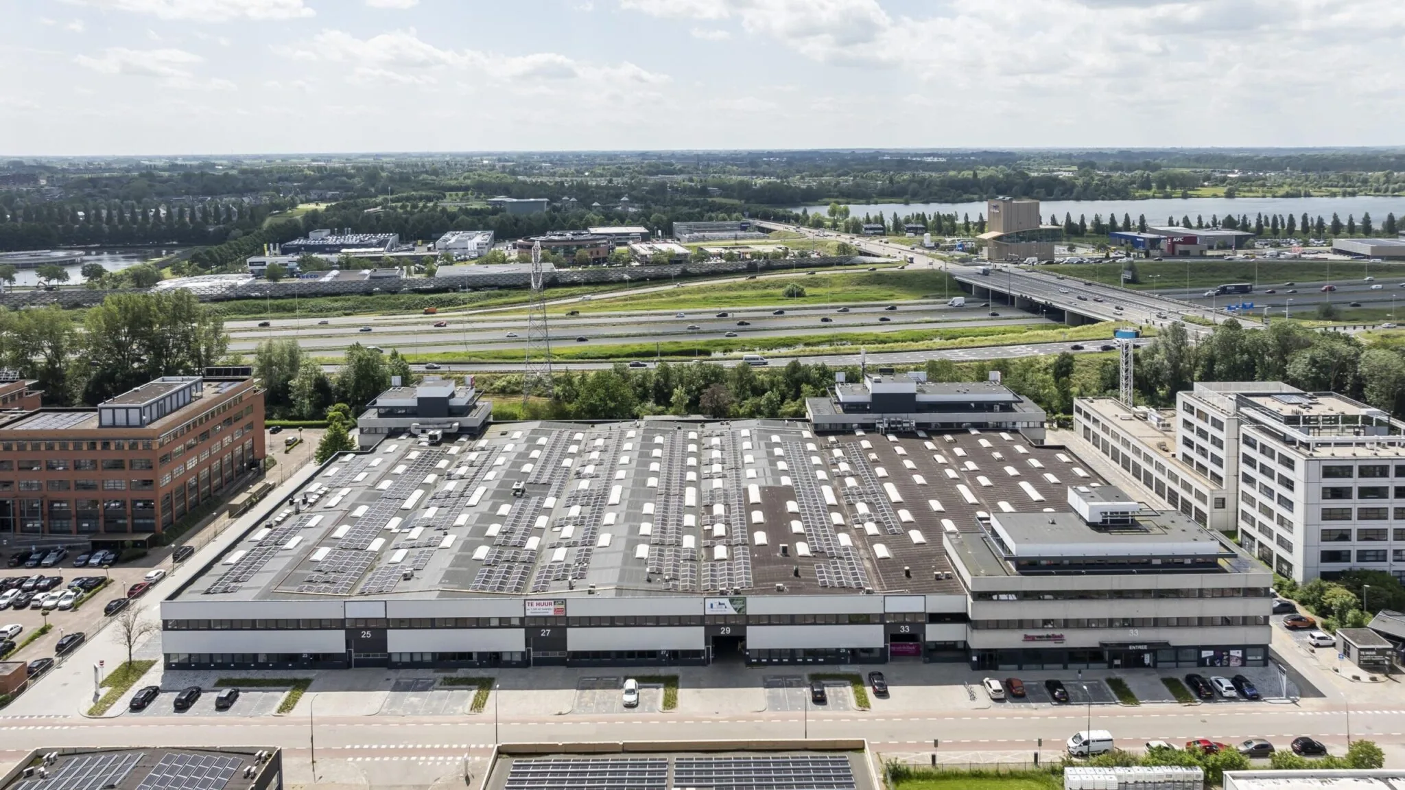 Luchtfoto van een bedrijfspand aan de Zonnebaan in Utrecht met zonnepanelen op het dak, gelegen naast de snelweg.