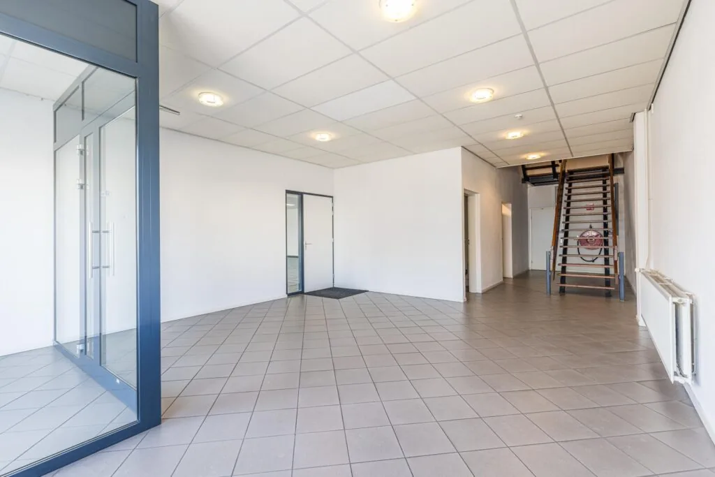 Lichte entreehal met tegelvloer, glazen scheidingswand en houten trap in een bedrijfsgebouw aan de Zonnebaan.