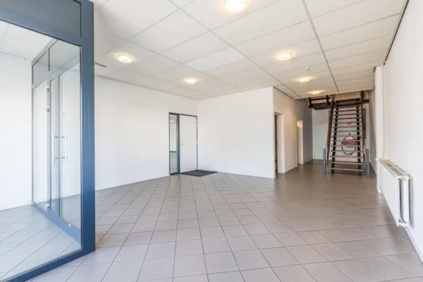 Lichte entreehal met tegelvloer, glazen scheidingswand en houten trap in een bedrijfsgebouw aan de Zonnebaan.