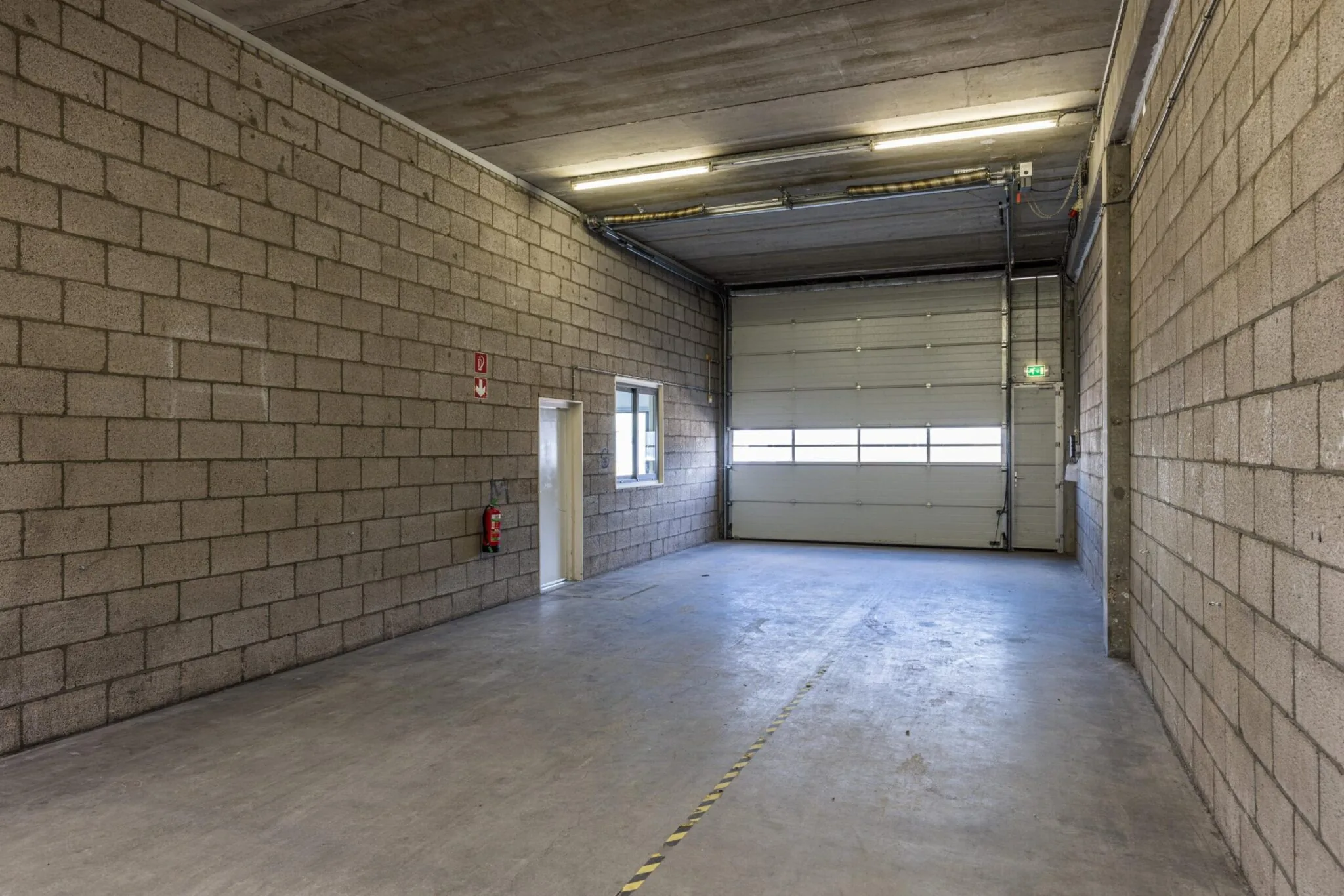 Leegstaande bedrijfsruimte aan de Zonnebaan met betonnen vloer, stenen muren en een grote overheaddeur.