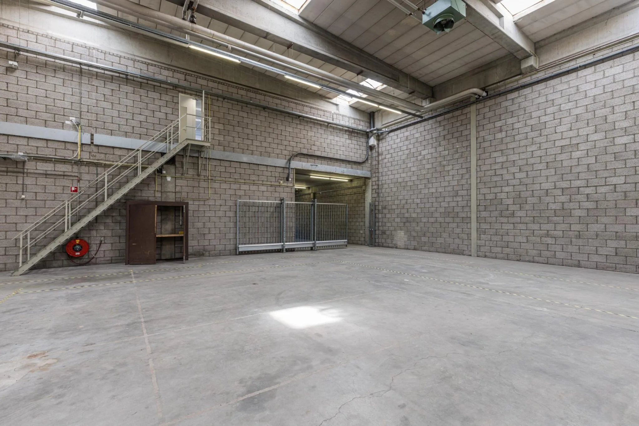 Leeg industrieel magazijn aan de Zonnebaan met betonnen vloer, trap en overheaddeur.