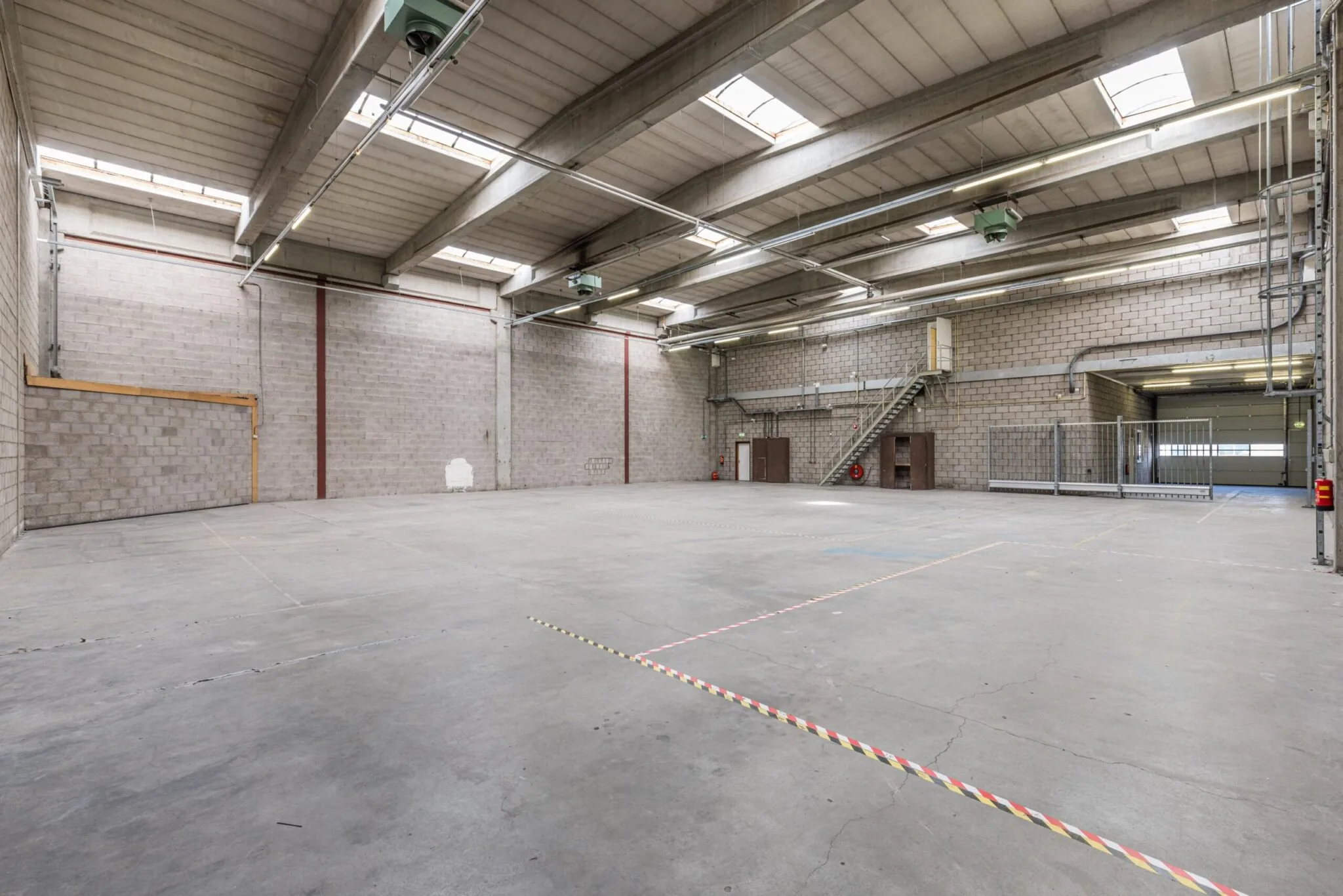 Ruime, lege bedrijfsruimte aan de Zonnebaan met betonnen vloer, hoge plafonds en industriële afwerking.
