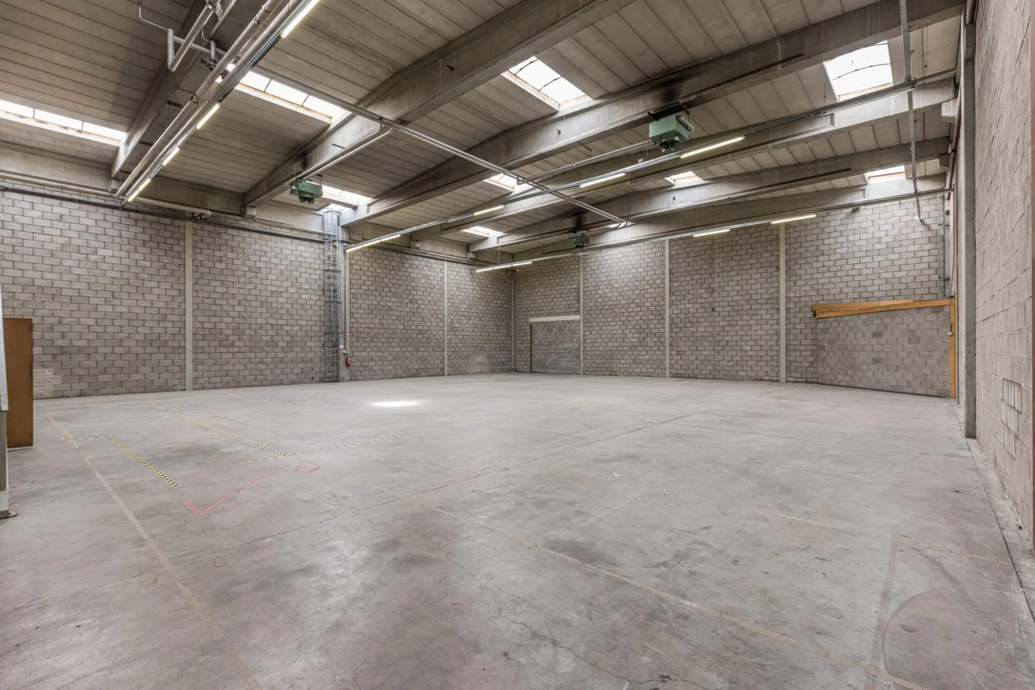 Lege, ruime bedrijfshal aan de Zonnebaan met betonnen vloer en muren, voorzien van dakramen en verlichting.
