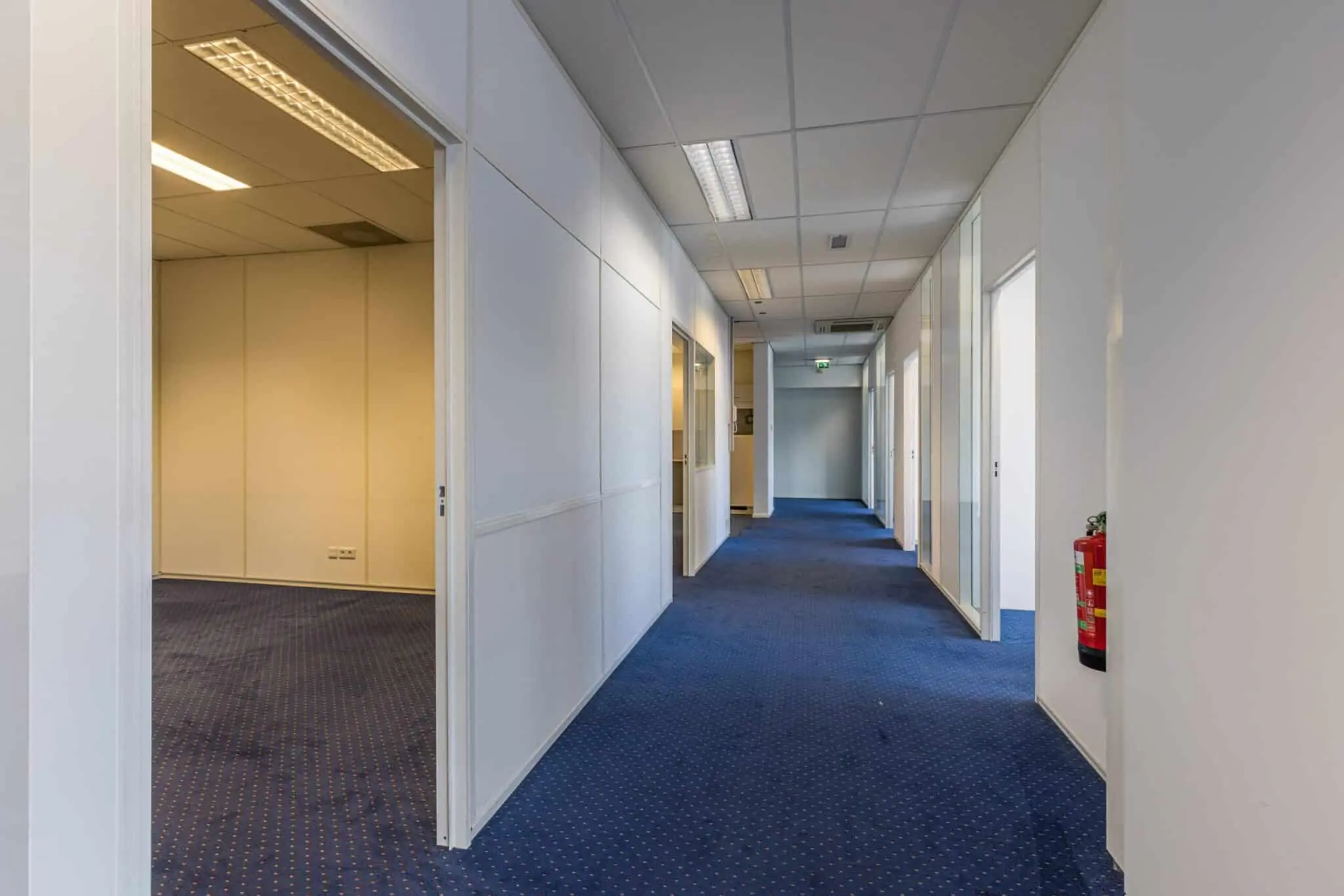 Gang met blauwe vloerbedekking en meerdere kantoordeuren in een bedrijfsverzamelgebouw aan de Zonnebaan.