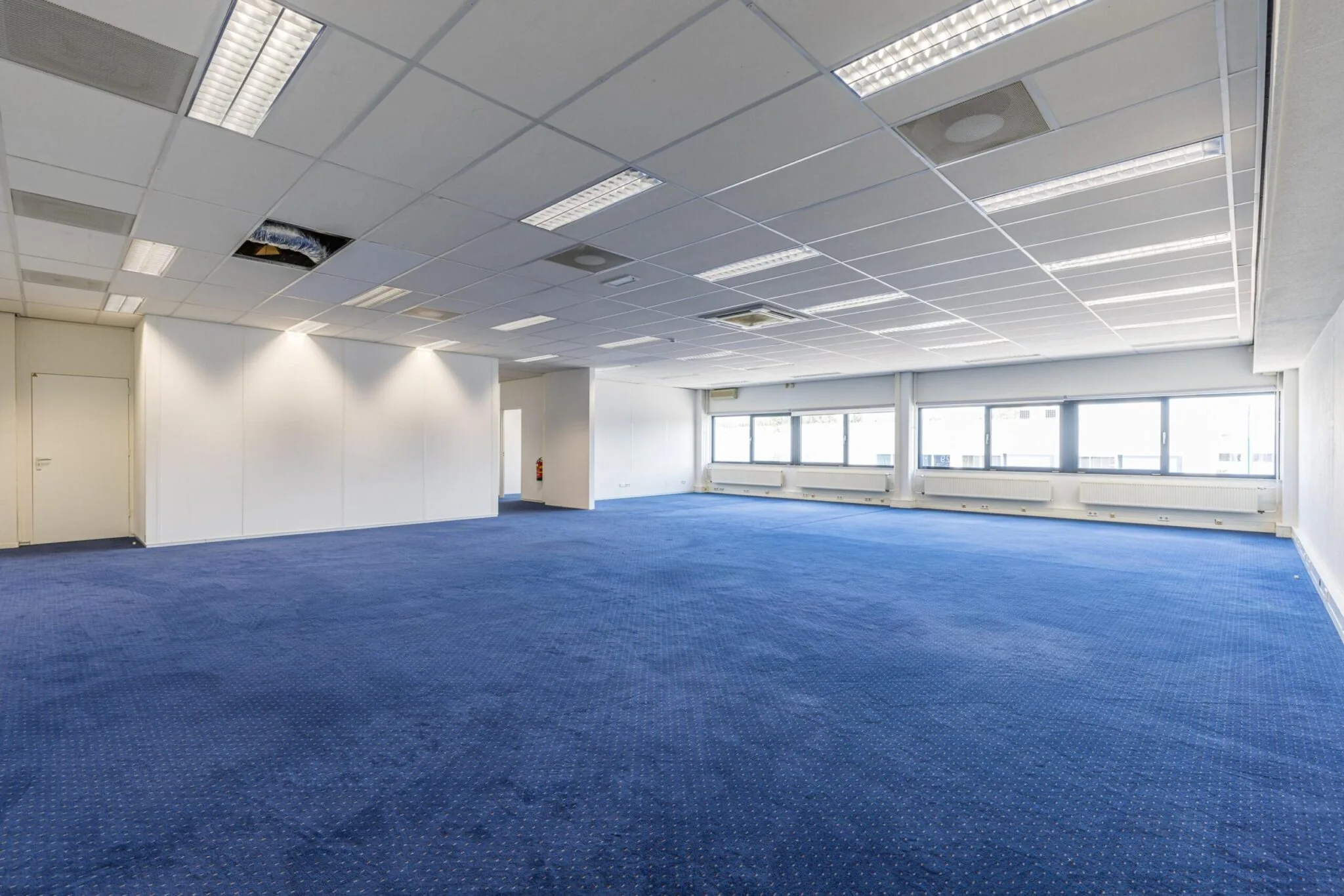 Leeg kantoorpand aan de Zonnebaan met blauwe vloerbedekking en systeemplafond.