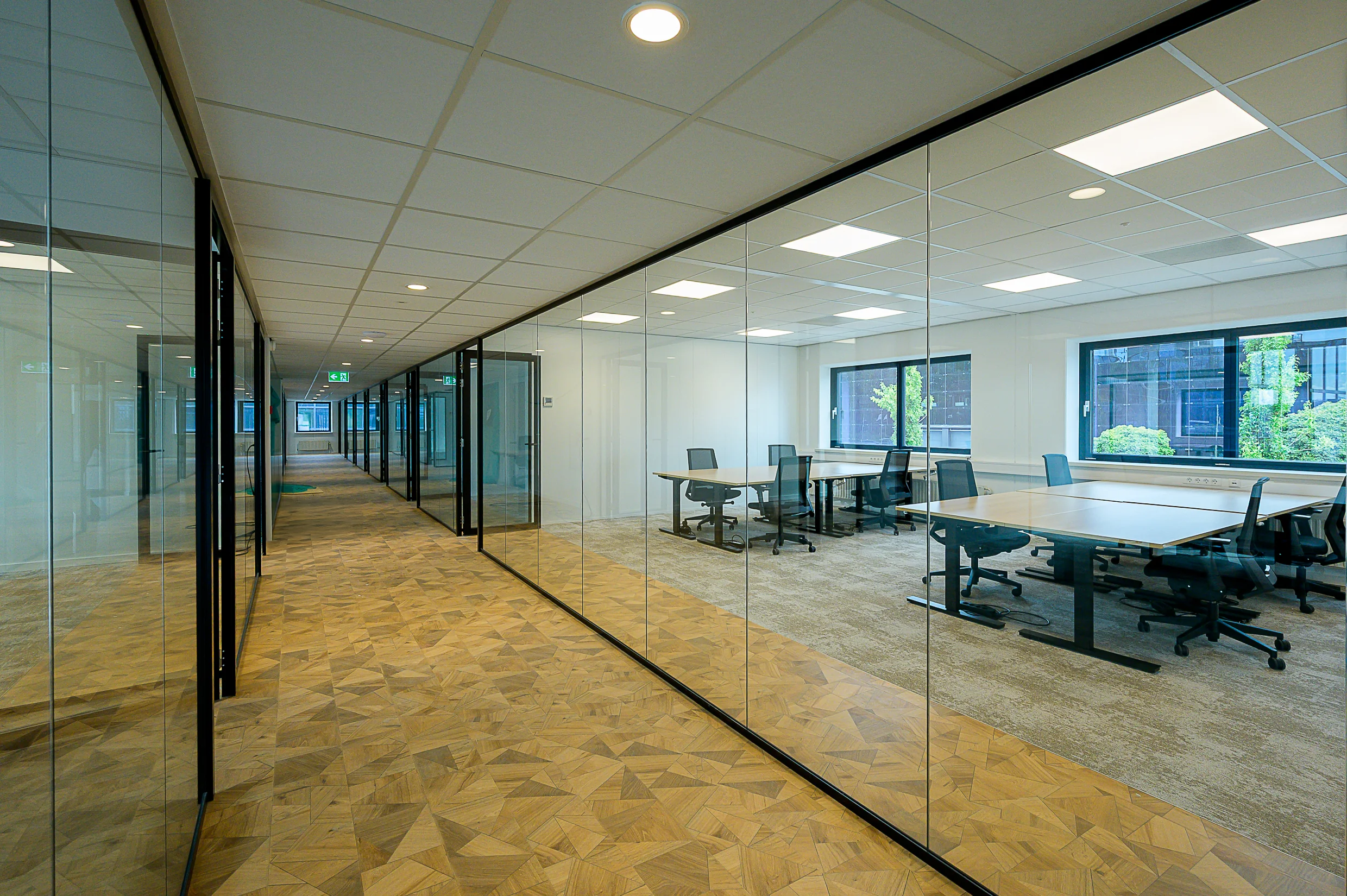 Modern office hallway with glass-walled meeting rooms and desks at Essebaan.